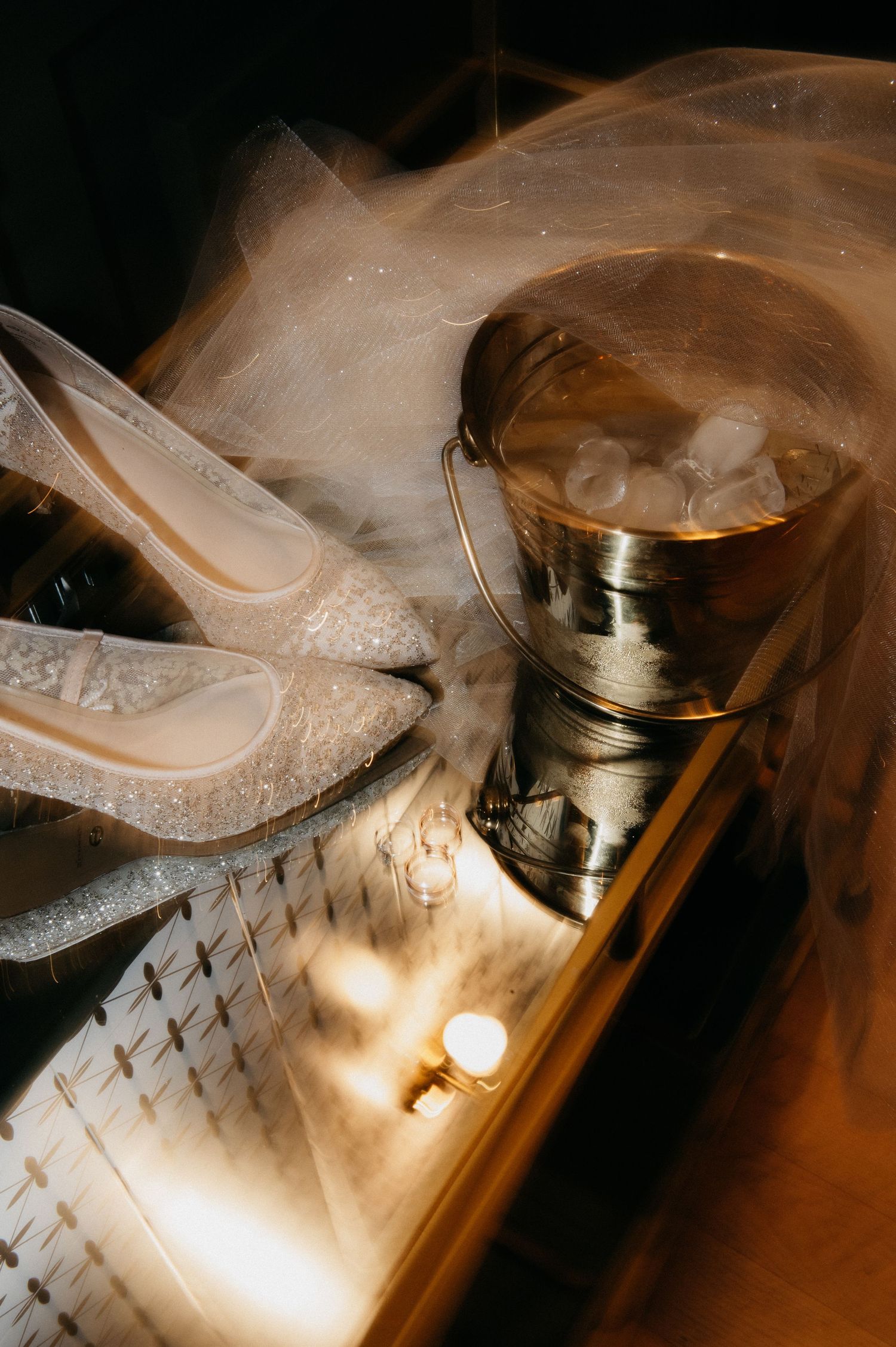 Elegant bridal details featuring sparkly heels, a sheer veil, and a gold ice bucket in warm golden light.