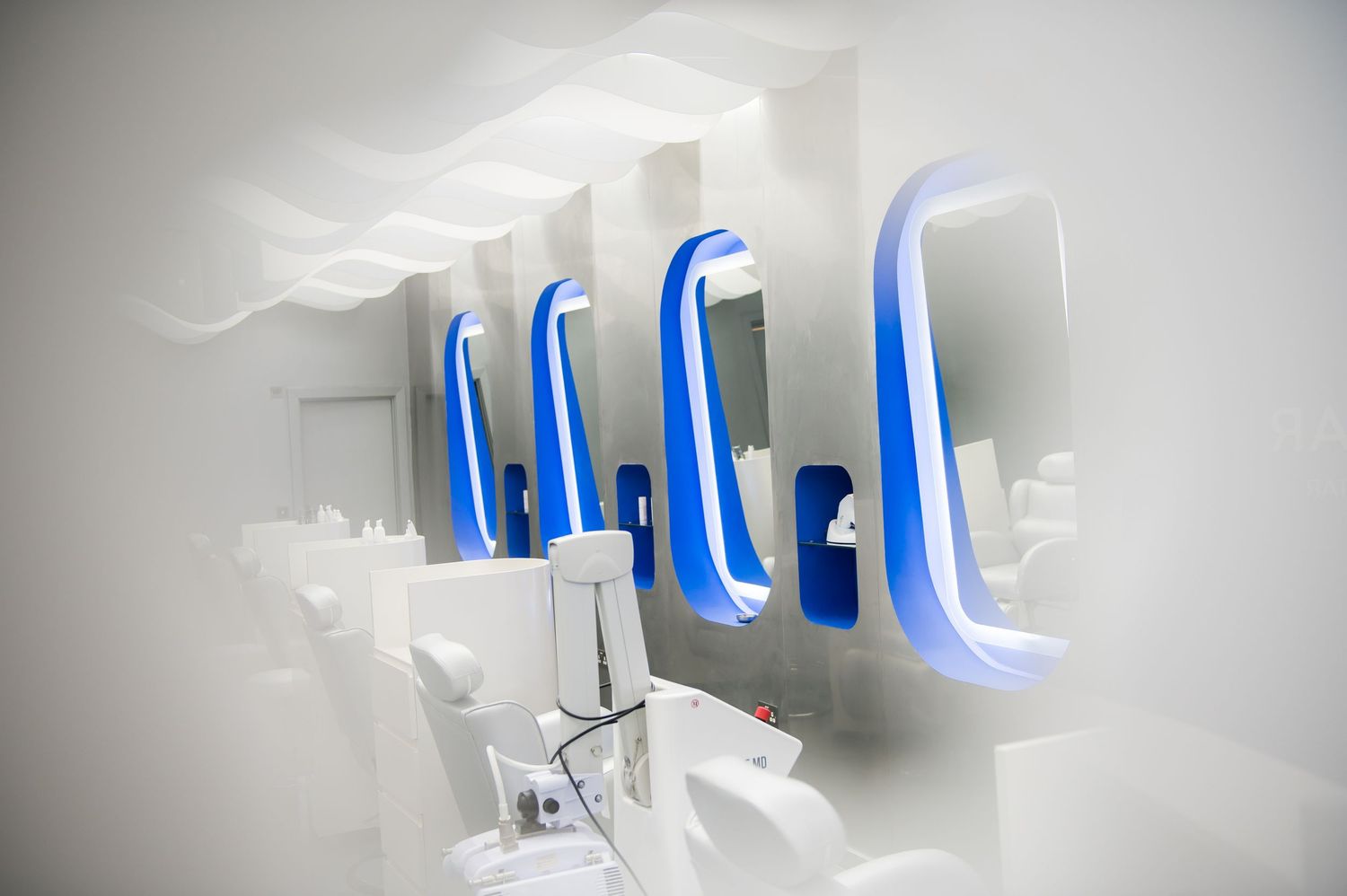 Modern white salon interior with blue neon-lit mirrors and sleek styling stations in a futuristic design.