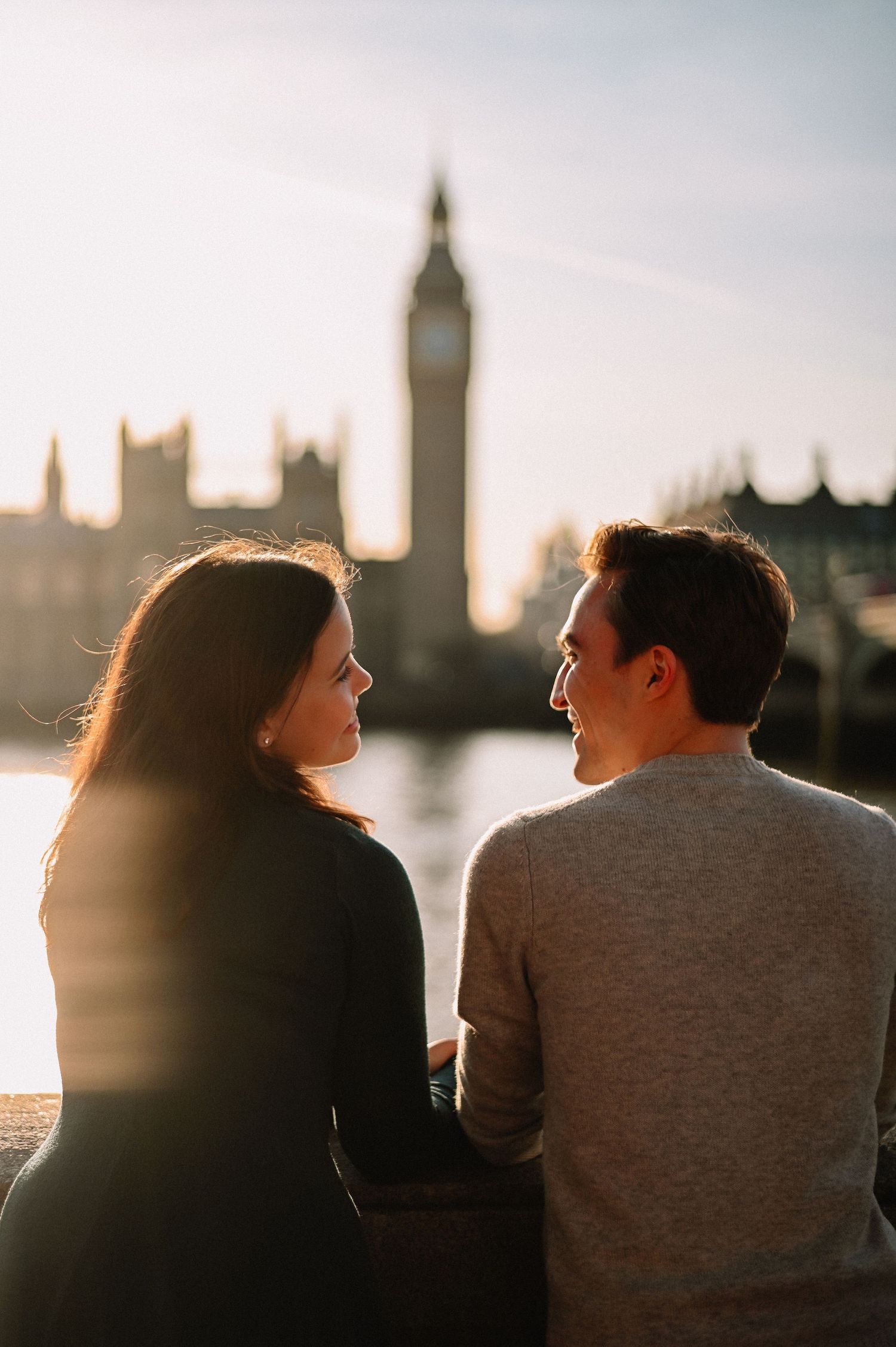 Couple sitting together by the Thames River with Big Ben and Houses of Parliament at golden hour in London.