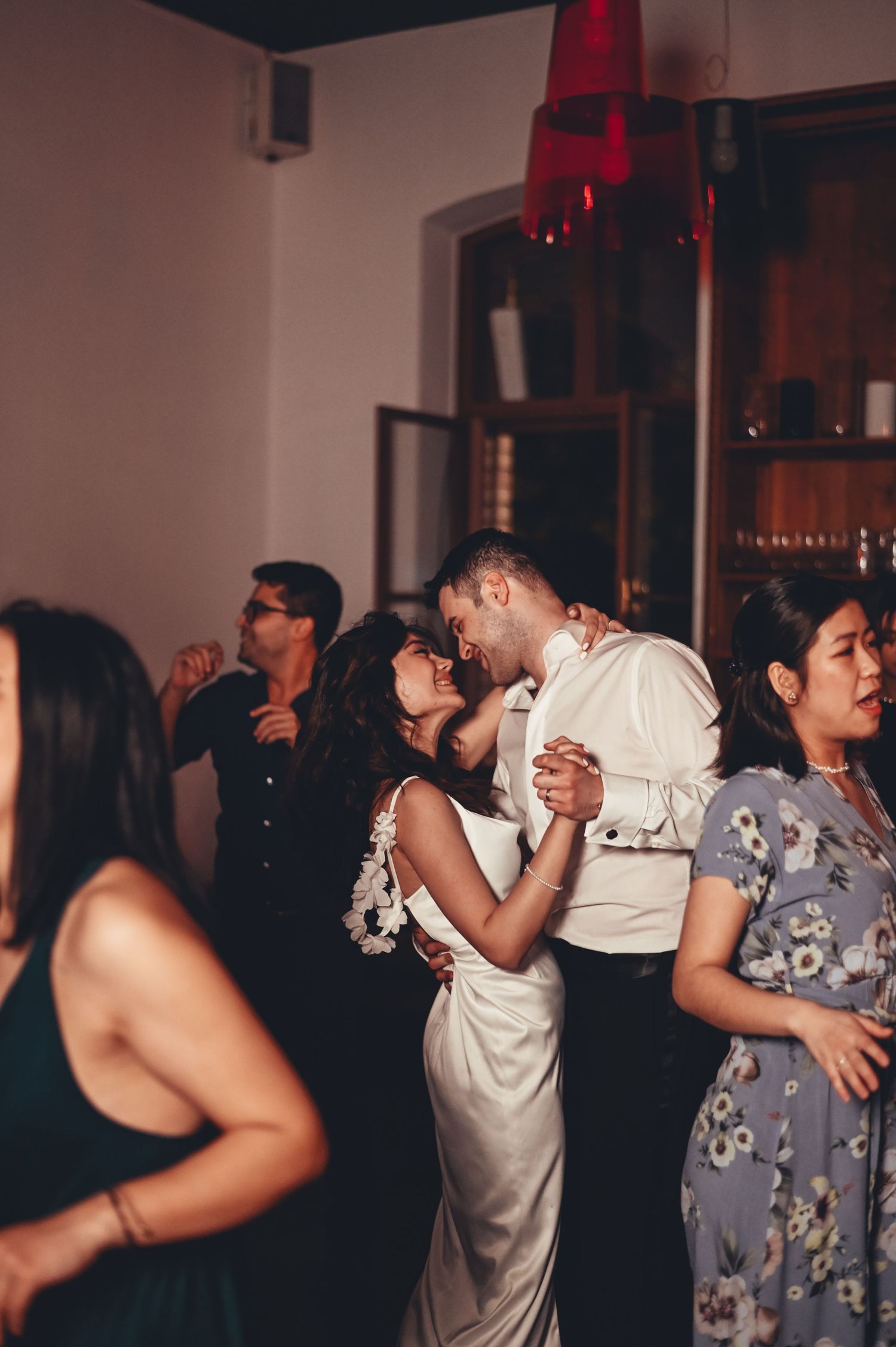 Bride and groom share a romantic kiss while dancing at their wedding reception surrounded by guests.