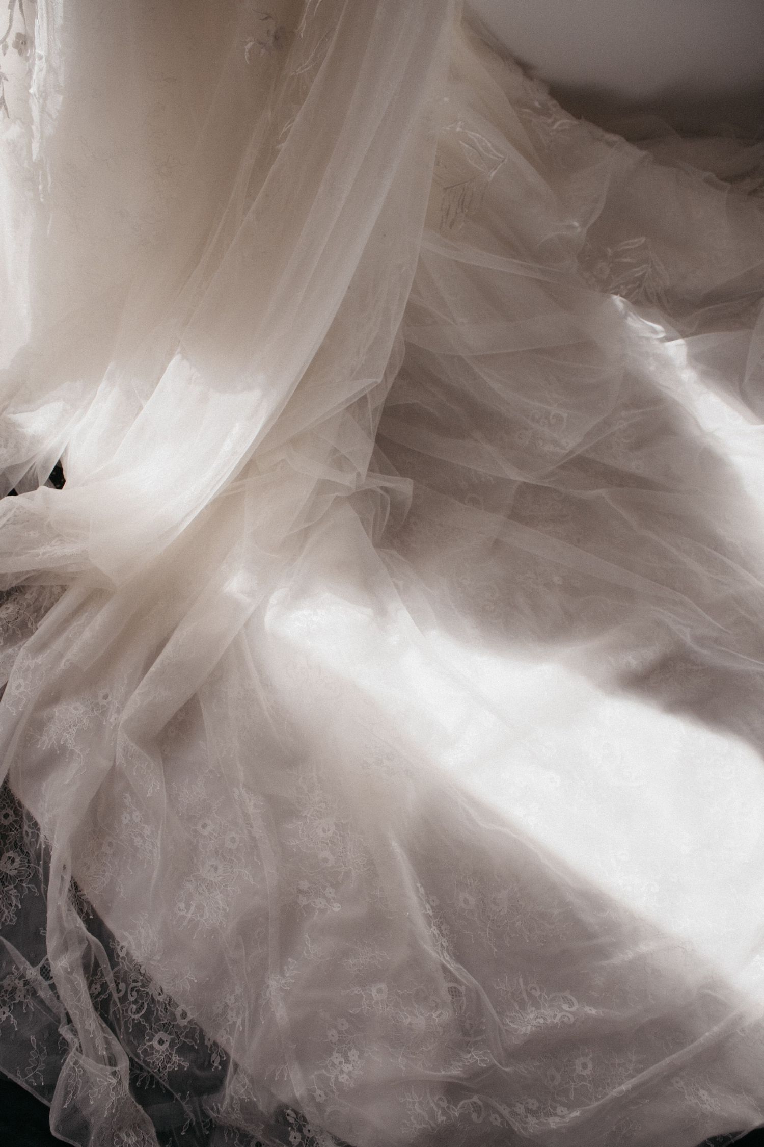 Soft white bridal gown with delicate lace and flowing tulle fabric draped elegantly in natural light.