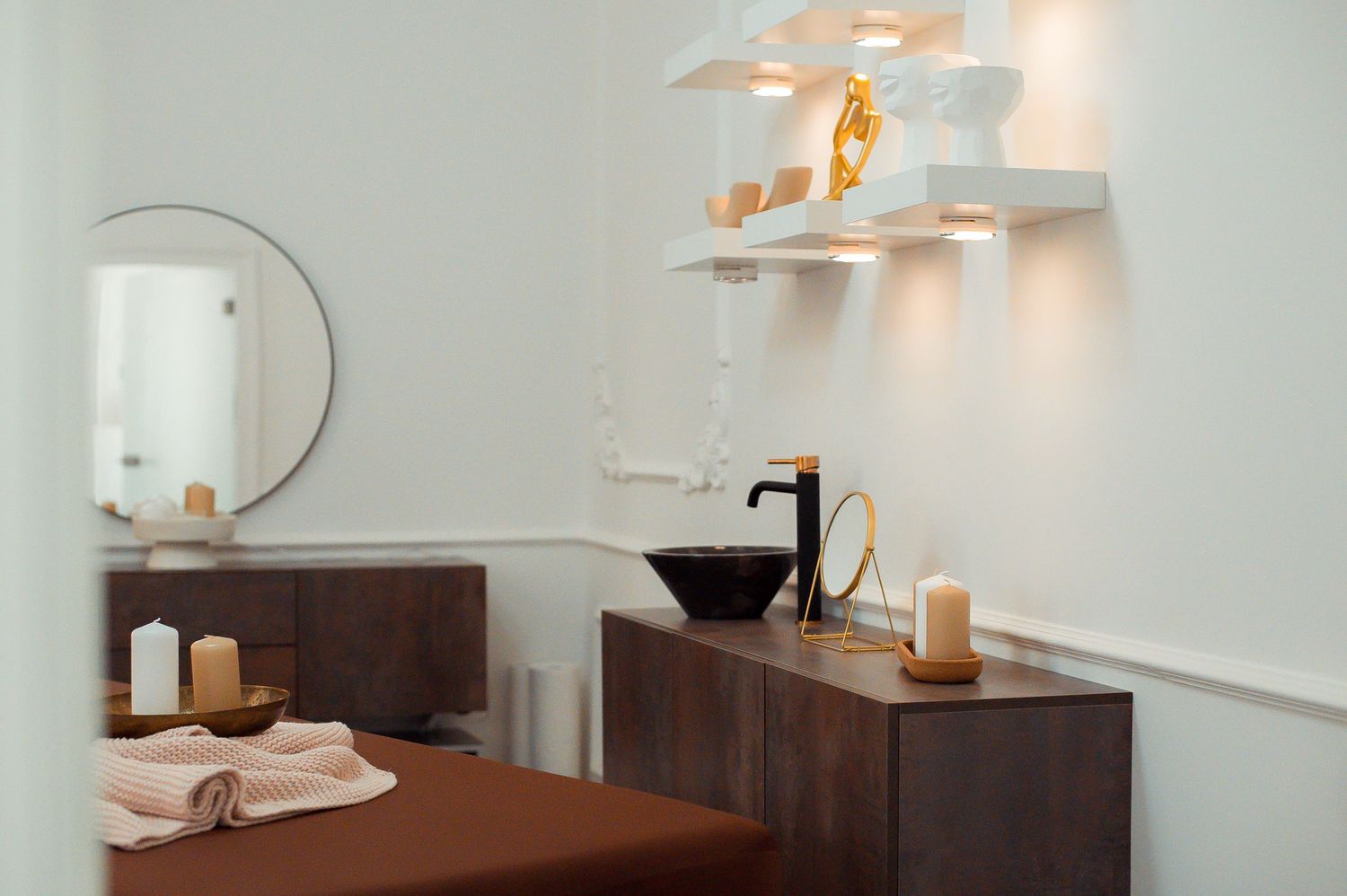 Elegant spa treatment room with wooden dresser, black basin, candles, and decorative white chandelier.