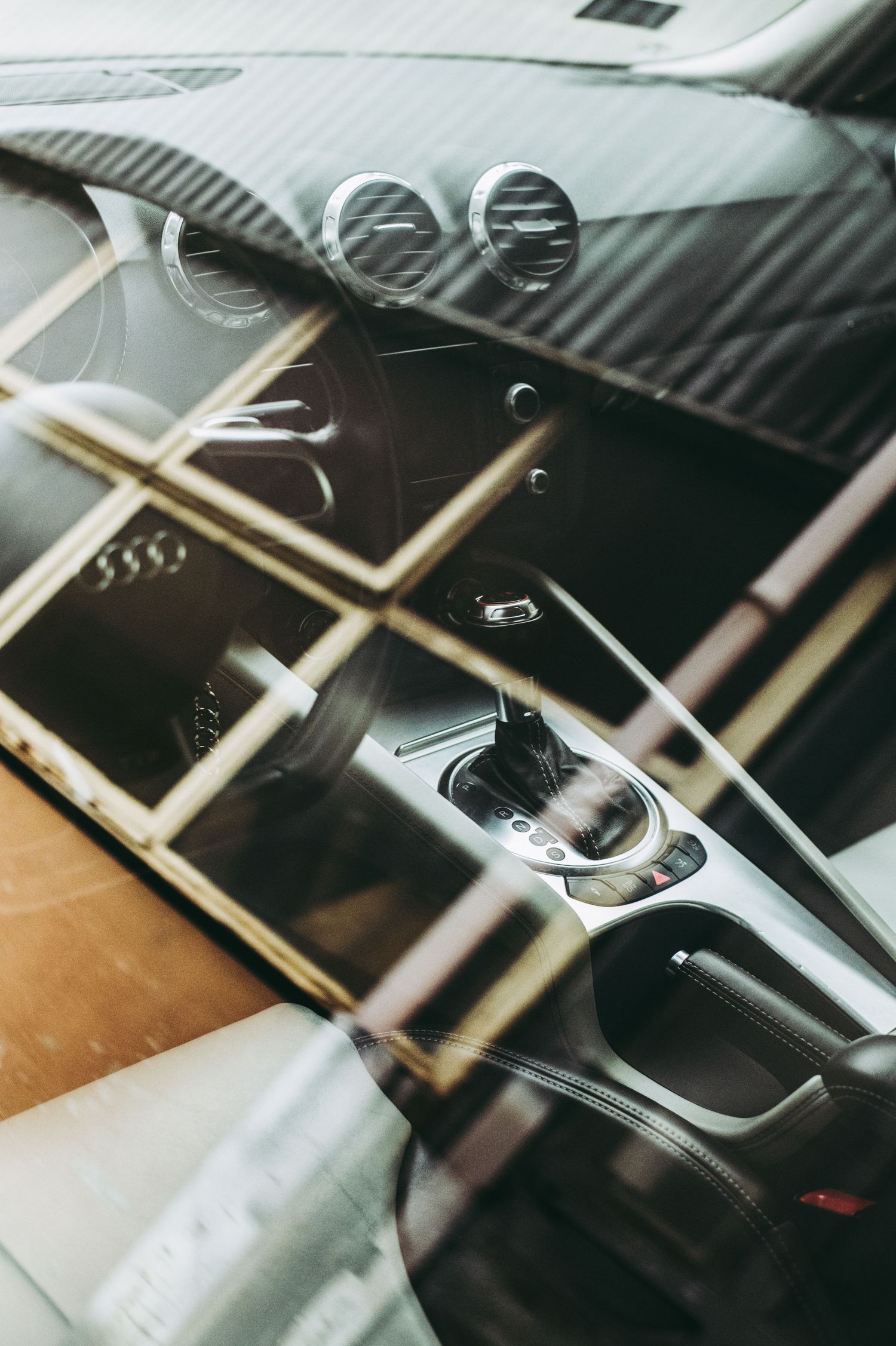 Close-up of a luxury car interior showing gear shift, center console, and air vents with reflective glass overlay.