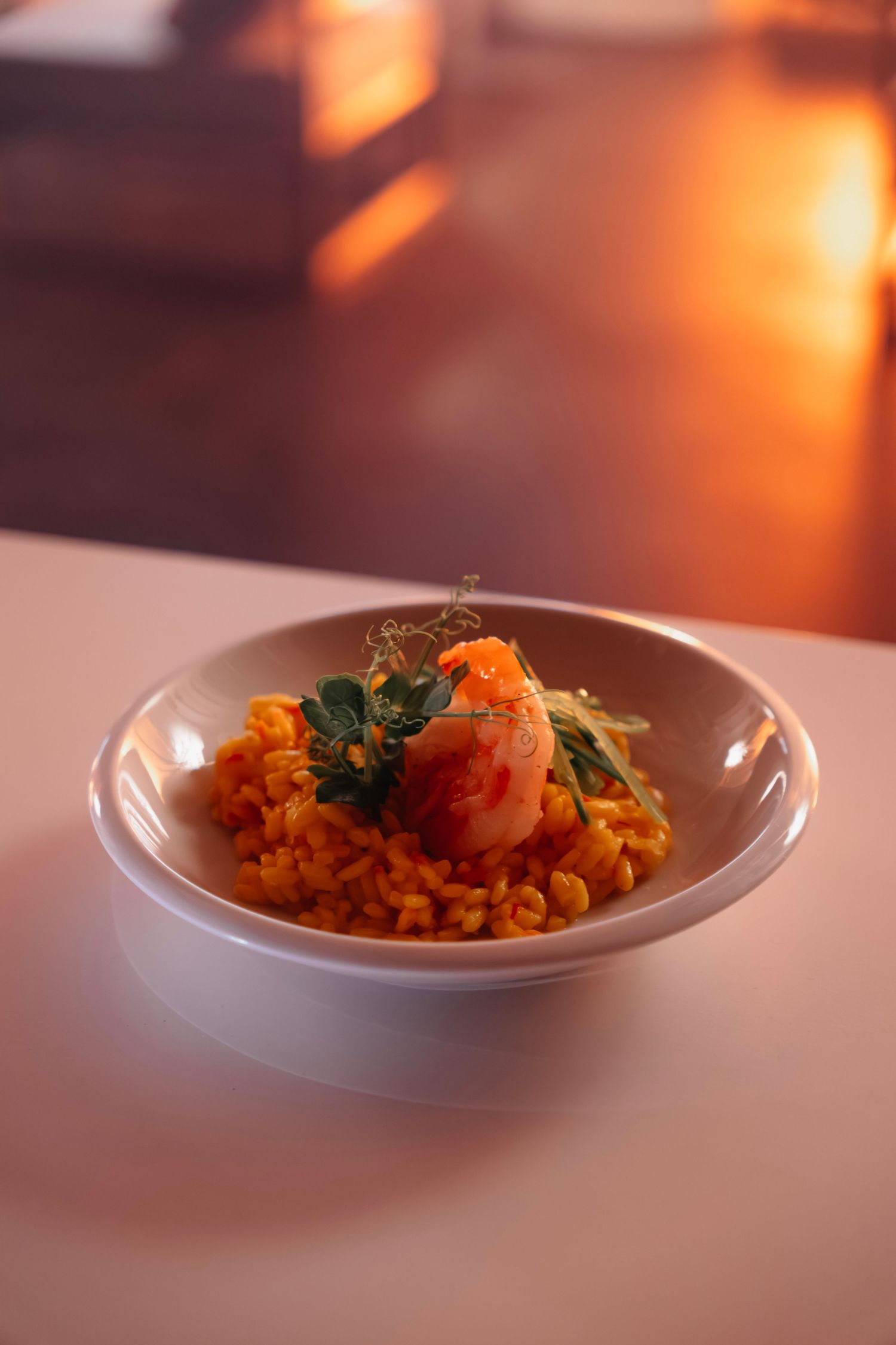 A bowl of saffron rice topped with a large shrimp and fresh herbs, served in warm ambient lighting.