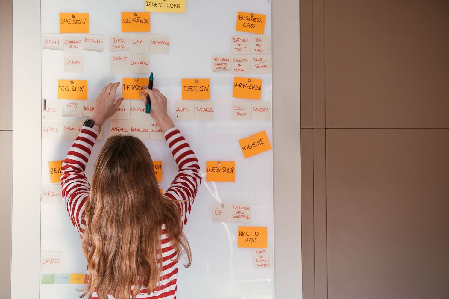 Woman in striped shirt organizing colorful sticky notes on a whiteboard during a business brainstorming session.