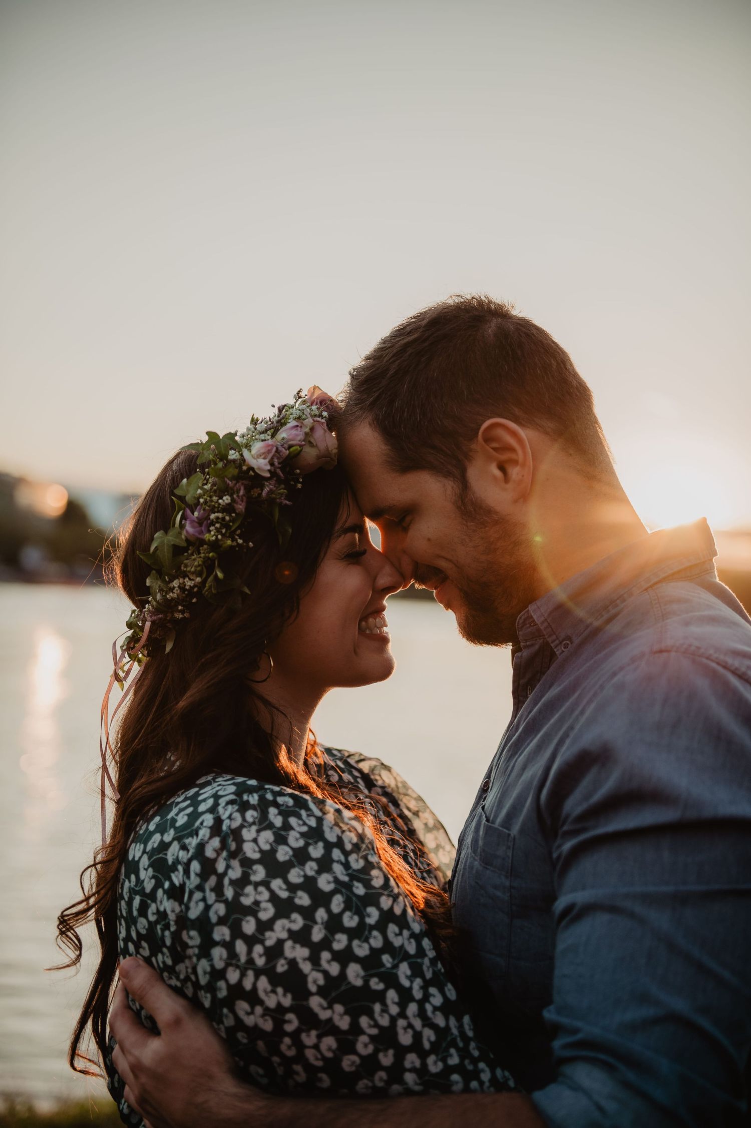 Romantic couple embracing forehead to forehead at golden sunset by a shimmering lake.