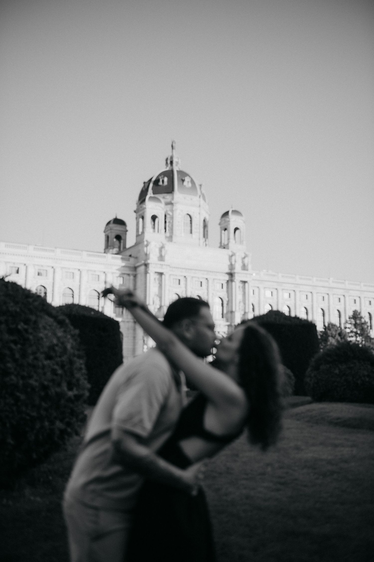Couple embracing in front of historic baroque building with dome in Vienna, captured in black and white photography.
