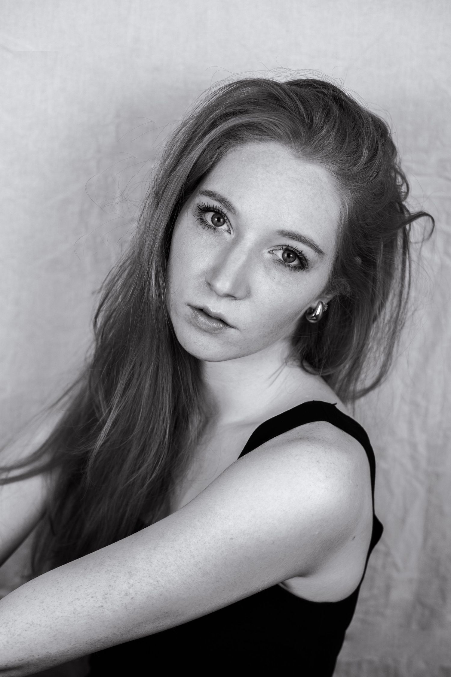 Black and white portrait of a young woman with long hair, freckles, and a small earring, wearing a black top.