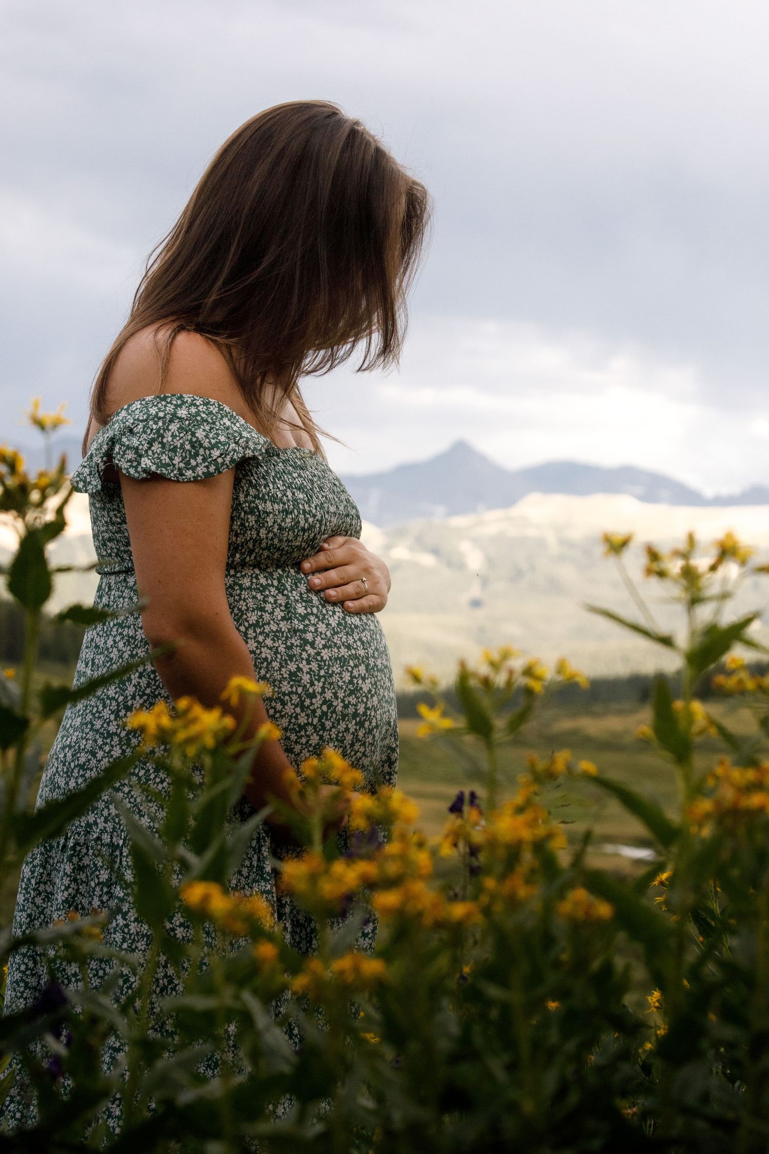Woman in floral dress standing in mountain wildflower field at sunset.