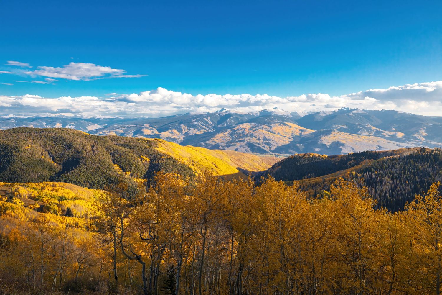 Panoramic view of mountain ranges under bright blue skies with scattered white clouds.