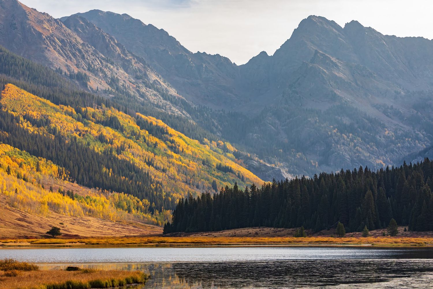 Snow-capped mountain peaks reflect in a tranquil alpine lake surrounded by golden autumn aspens.