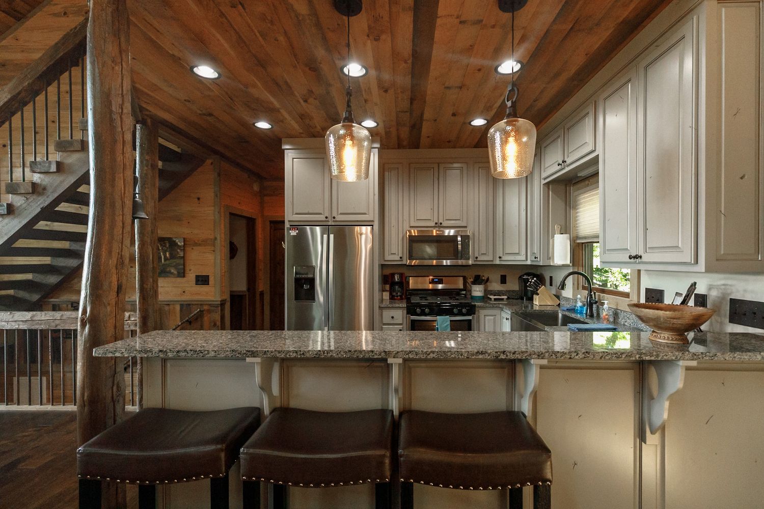 Modern kitchen interior with vaulted wooden ceiling, pendant lights, and stainless steel appliances.