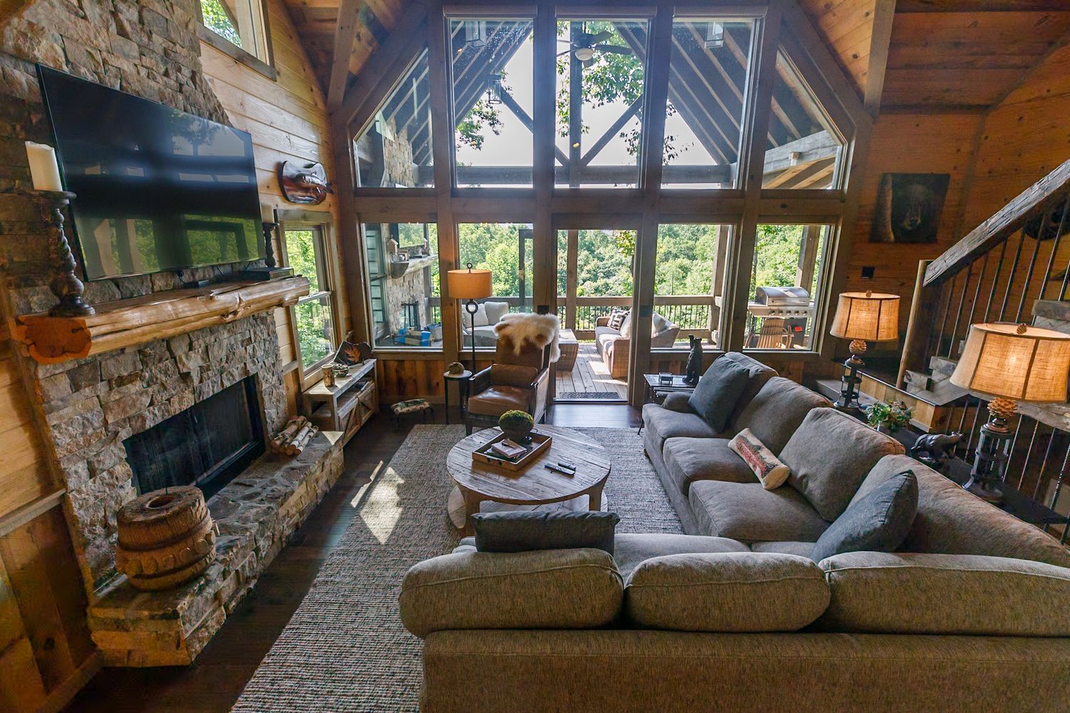 Luxurious mountain lodge living room with stone fireplace and large windows overlooking forest.