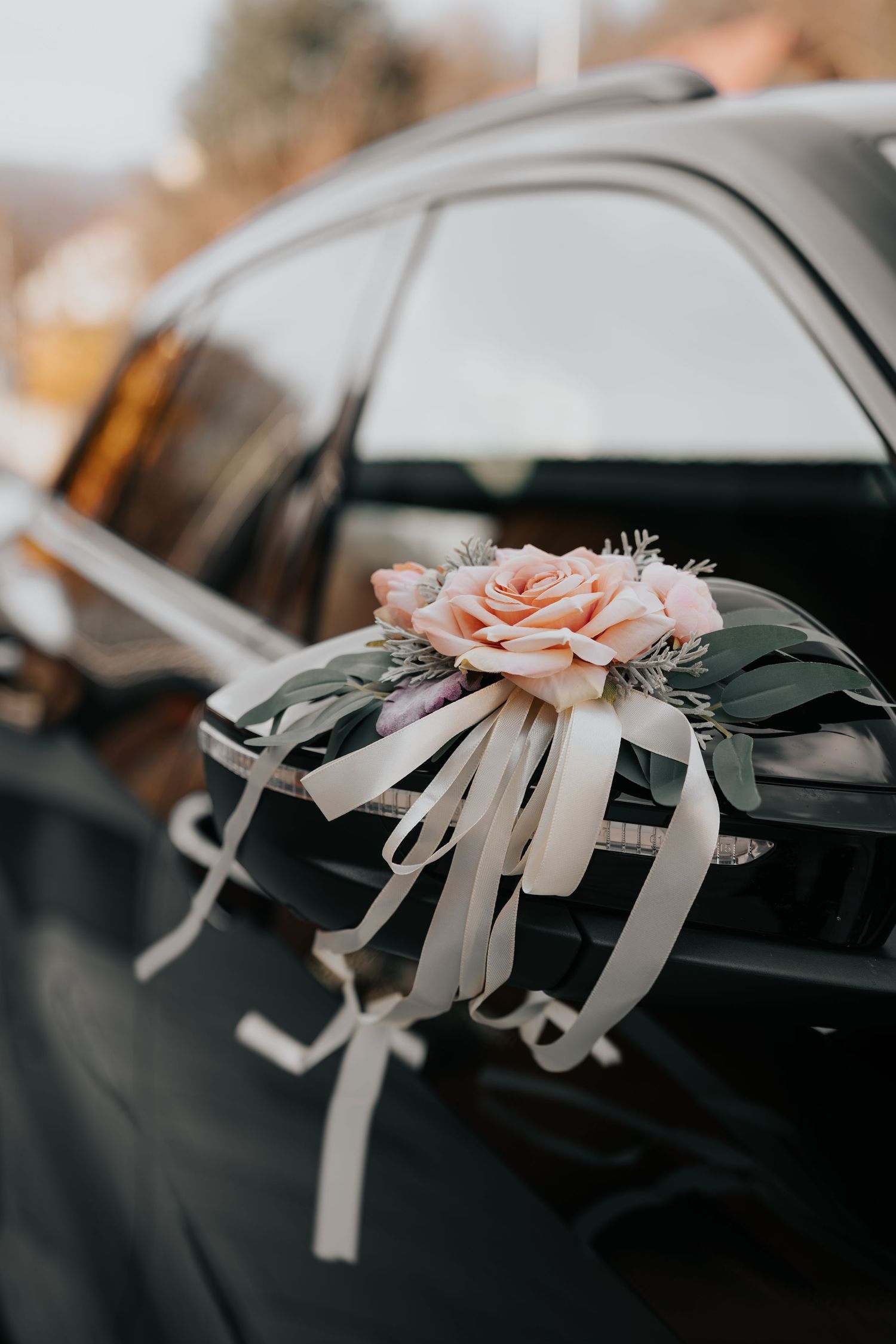 Black car adorned with a pink rose and white ribbon bow on the side mirror, perfect for a wedding decoration.