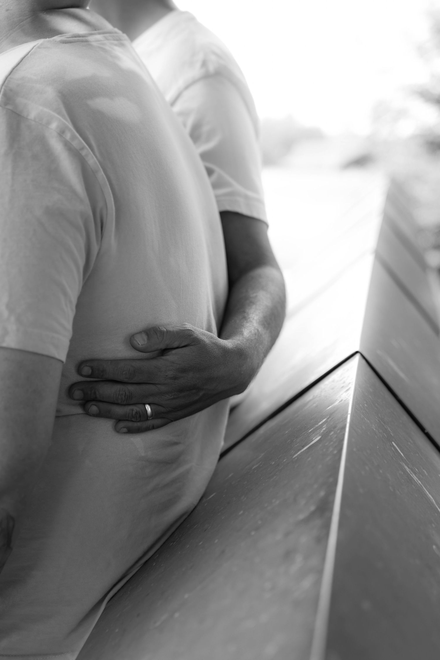 Black and white photo of a pregnant woman being embraced from behind, partner's hand resting on her baby bump.