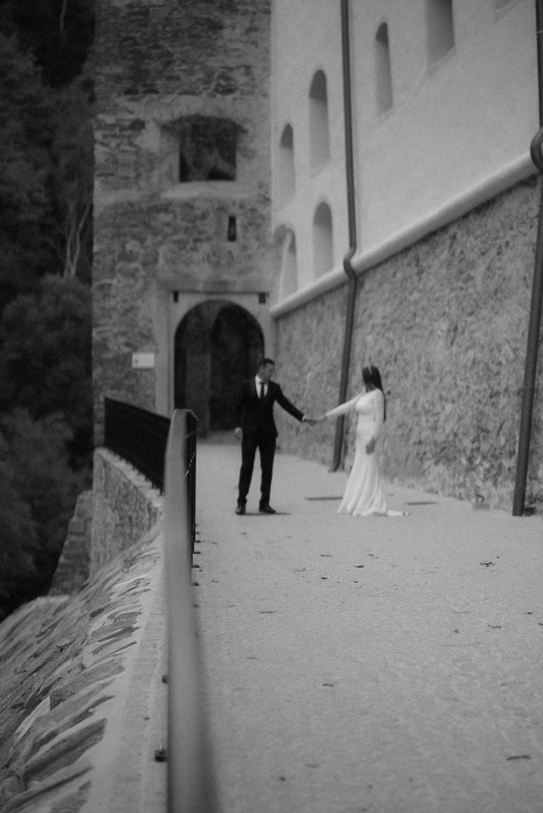 Black and white artistic wedding photo showing figures walking down a stone corridor with dramatic shadows.