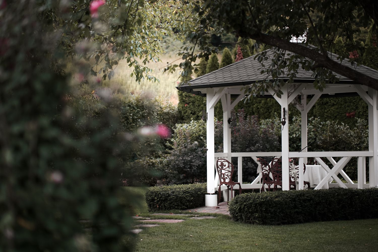 White gazebo structure surrounded by manicured gardens and trees.