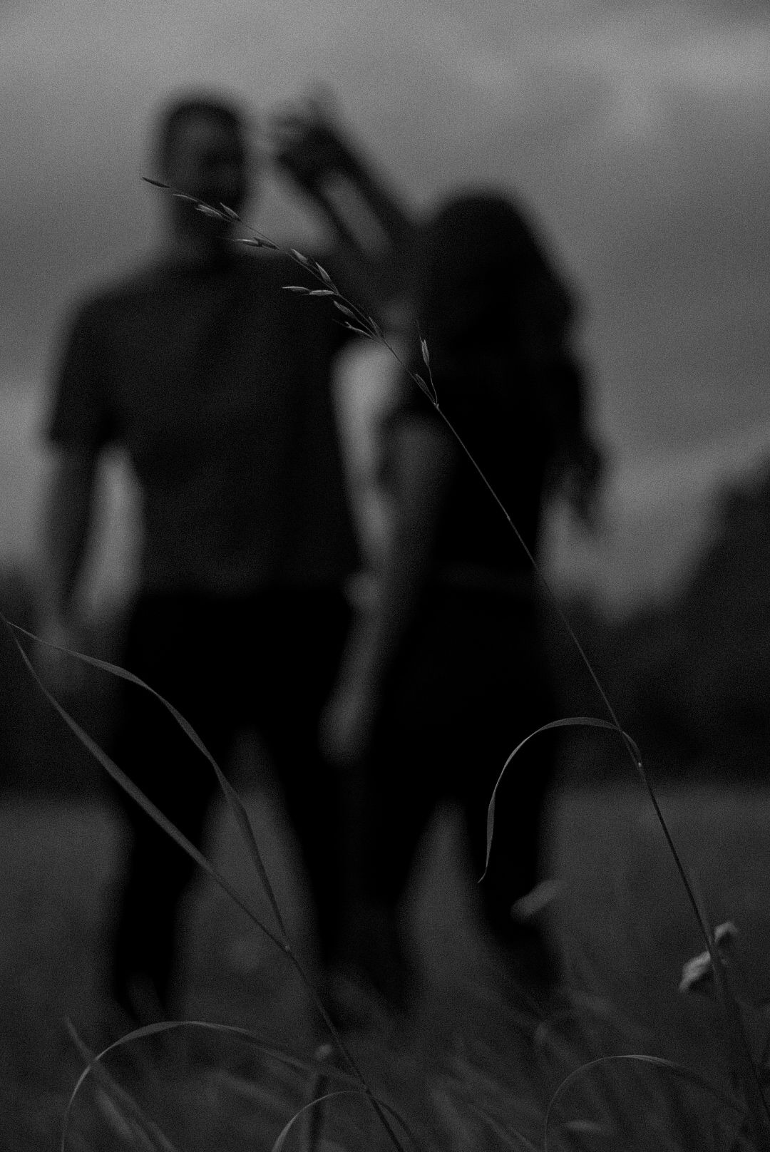 Black and white photo of a blurred couple dancing in a field with tall grass in the foreground.
