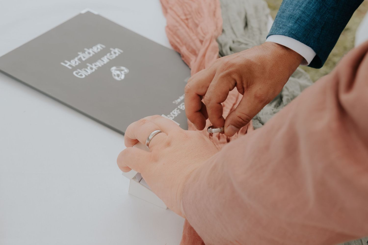 Close-up of wedding ring exchange with a gray wedding guest book in the background.