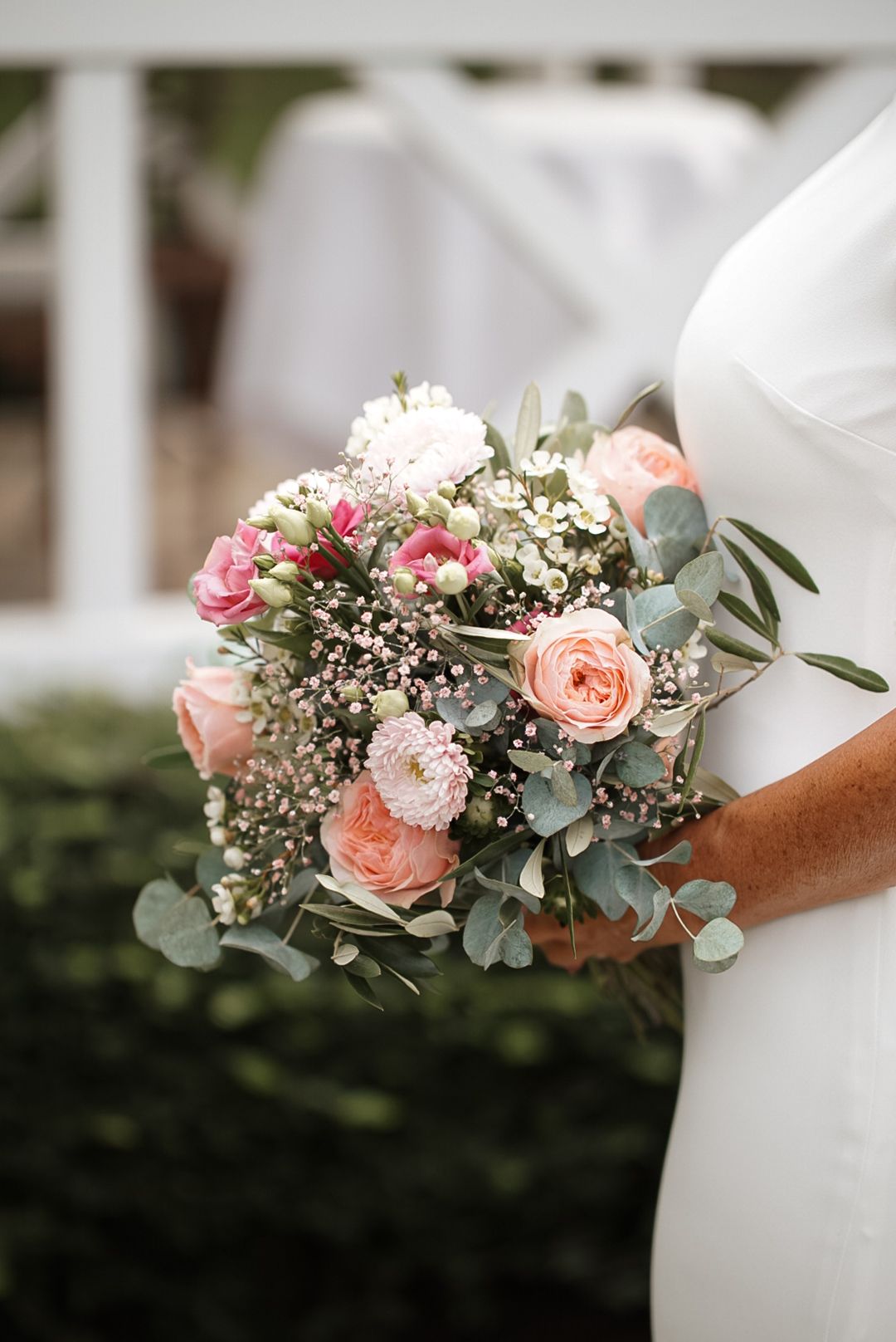 Close-up of a romantic bridal bouquet featuring peach roses, baby's breath, and eucalyptus leaves.