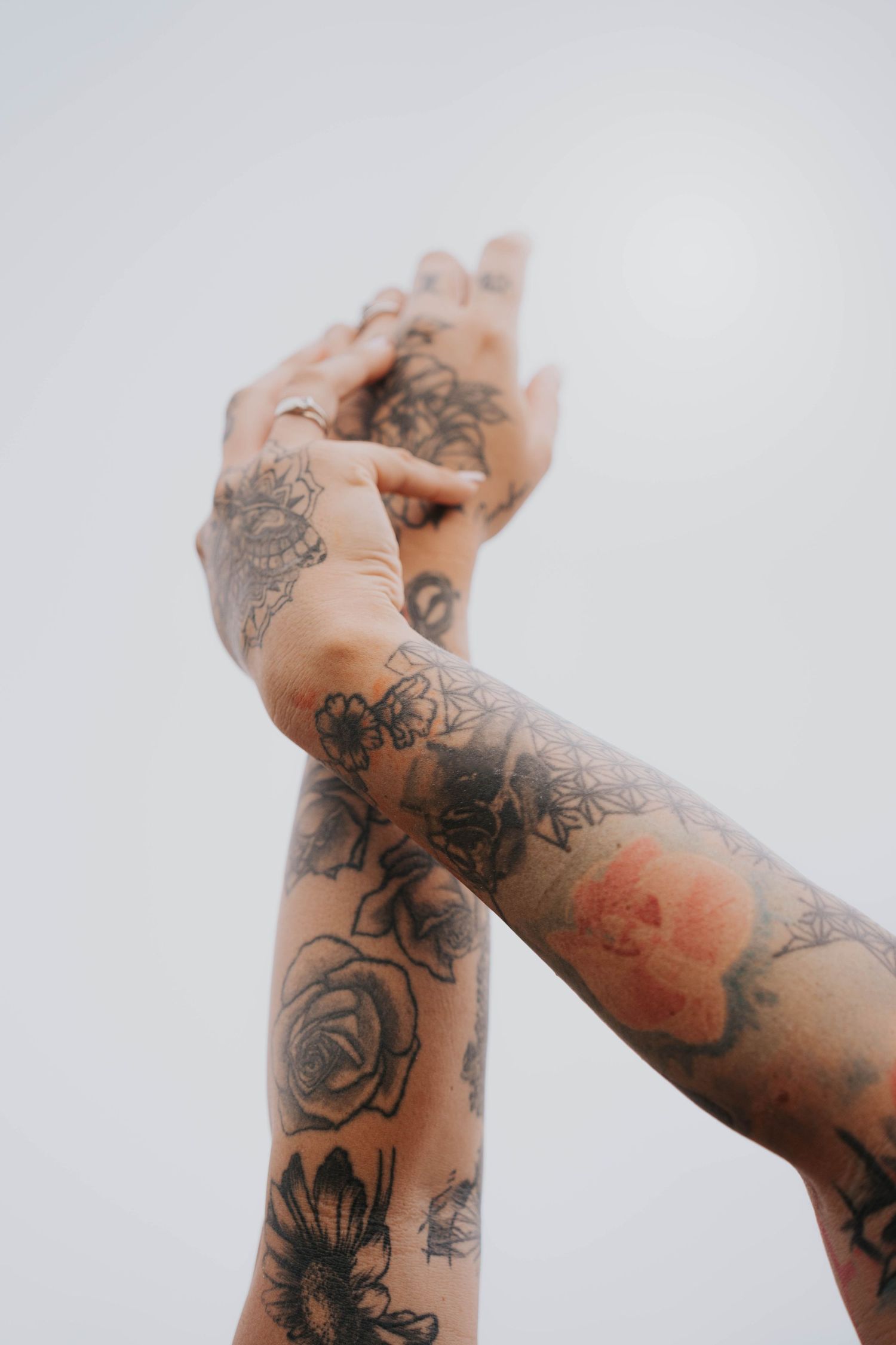 Two tattooed arms raised against a white sky, adorned with floral rose tattoo designs.