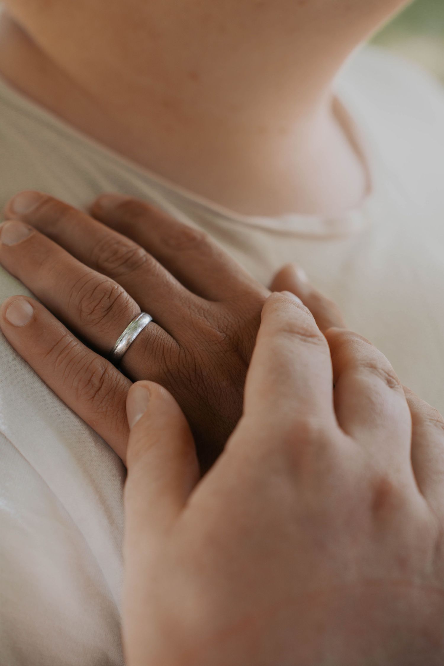 Close-up of hands with a silver wedding band resting on a person's chest in a tender moment.
