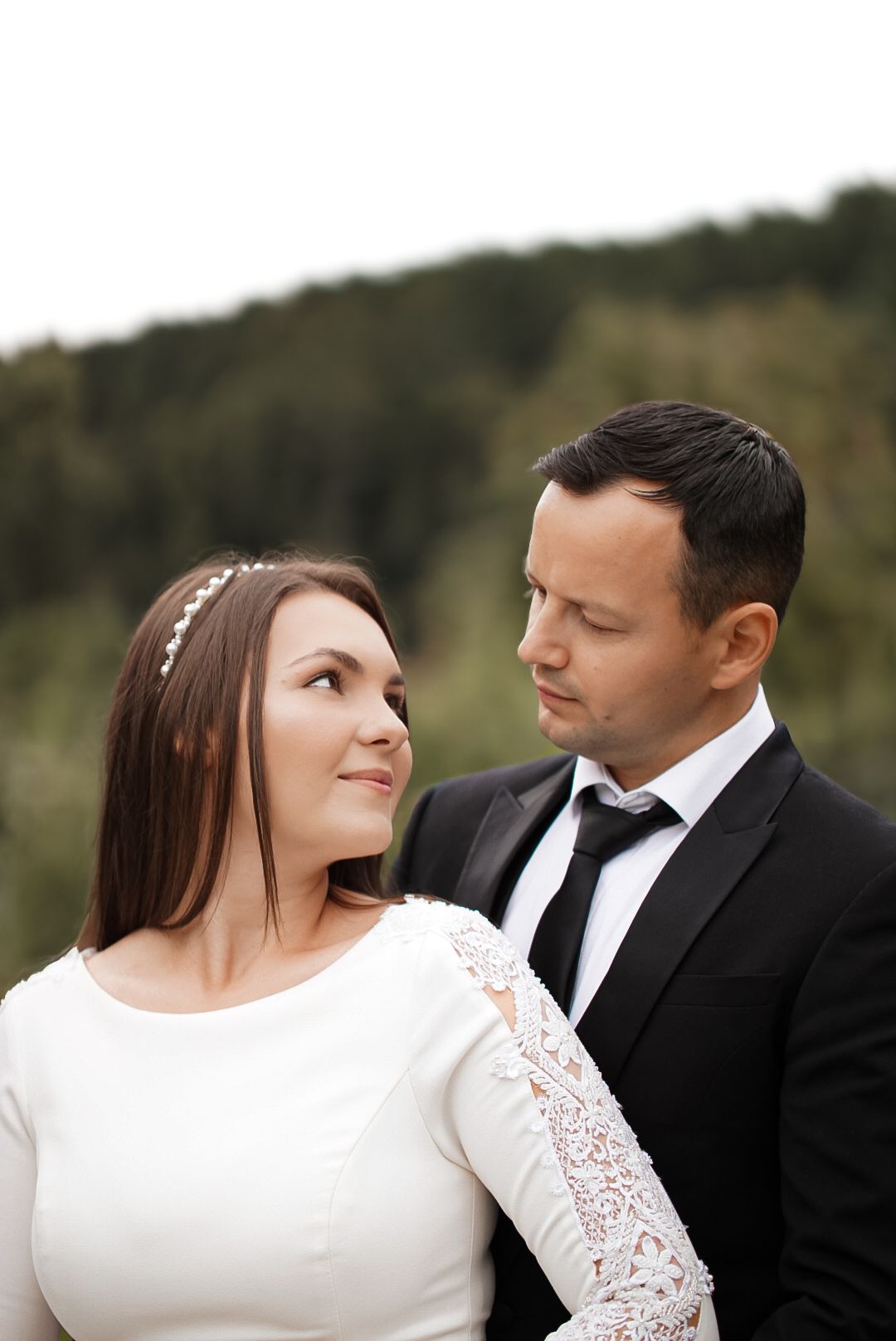 A bride and groom share a tender moment outdoors, with the bride in white lace and groom in a black suit and tie.