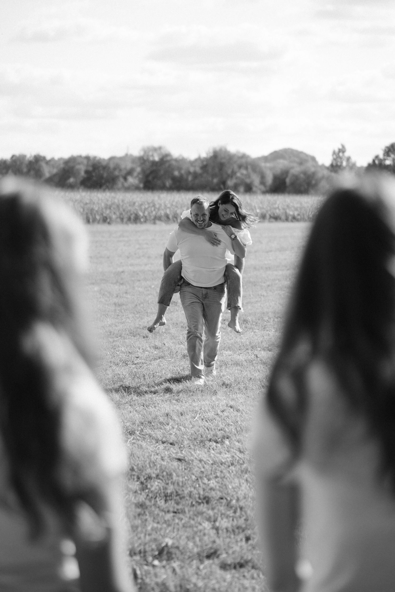 Black and white photo of a man giving a piggyback ride to a woman in an open field.