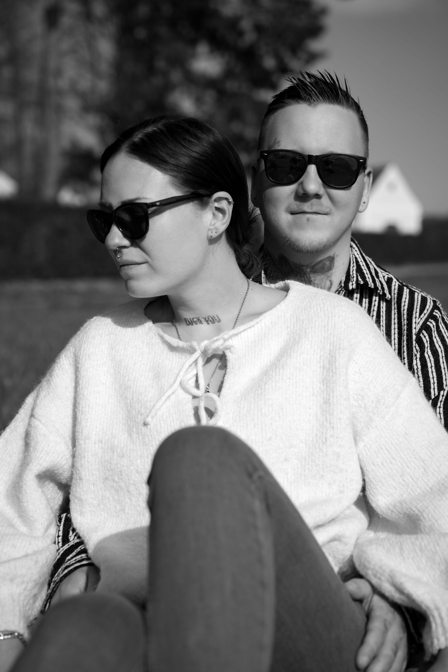 Black and white photo of a stylish couple wearing sunglasses sitting outdoors on a sunny day.