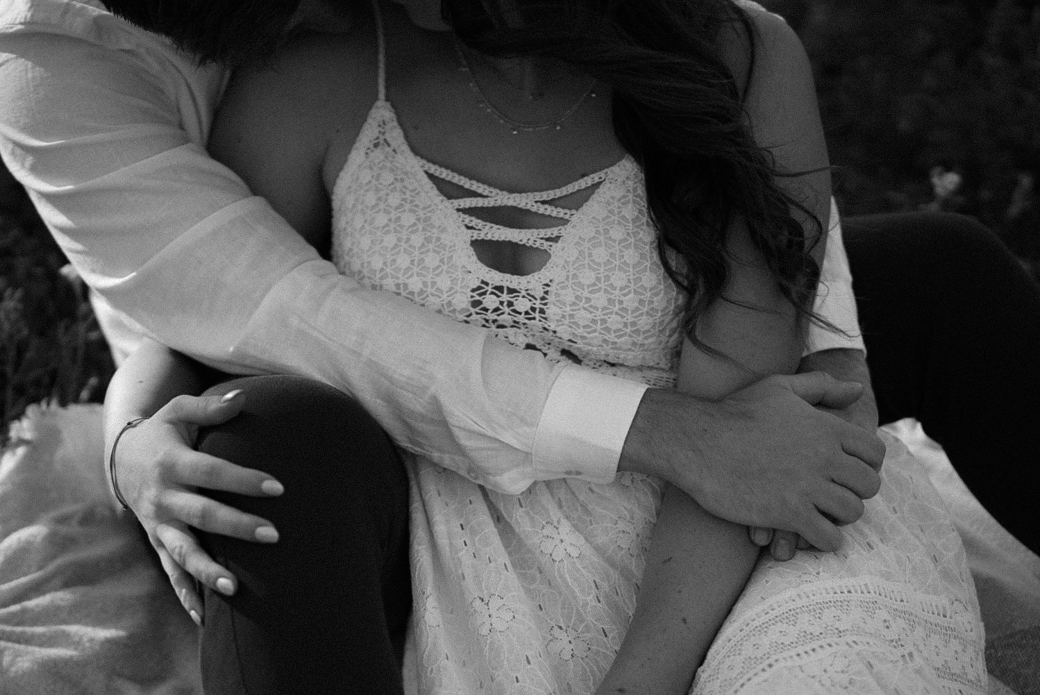 Black and white photo of a couple embracing, woman in white lace dress with man's arms wrapped around her.