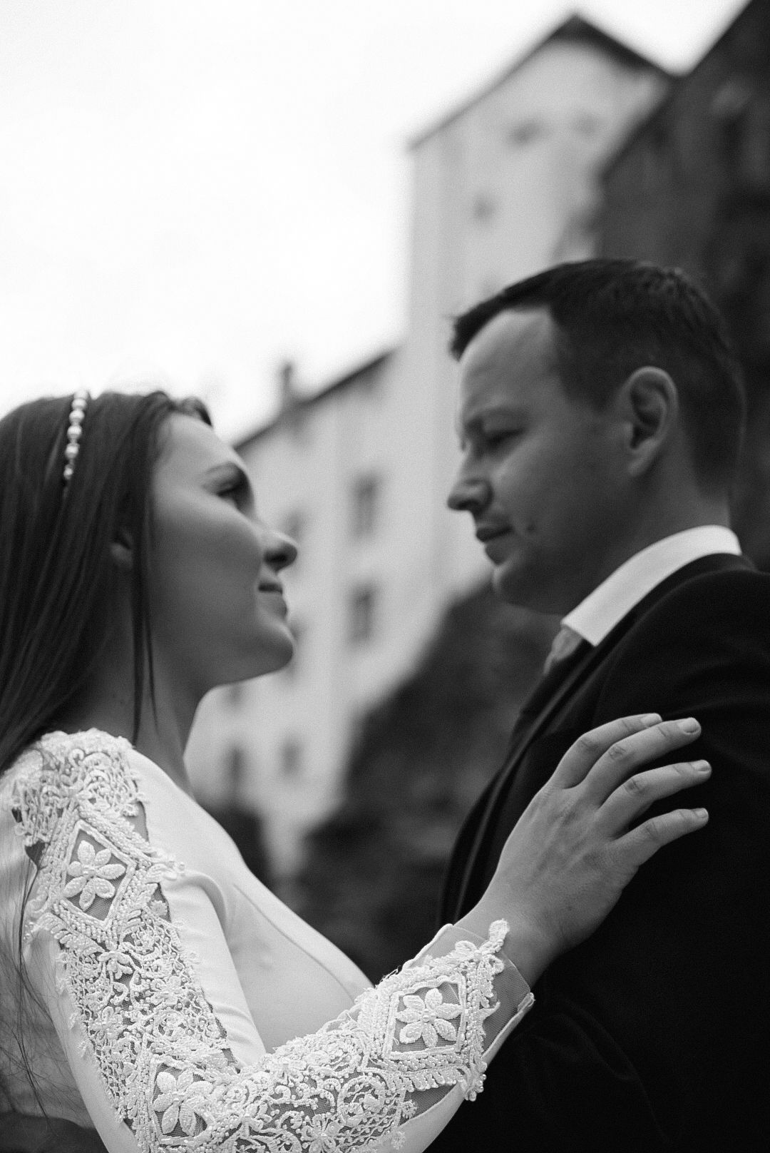 Black and white wedding photo of bride and groom gazing at each other near a historic building.