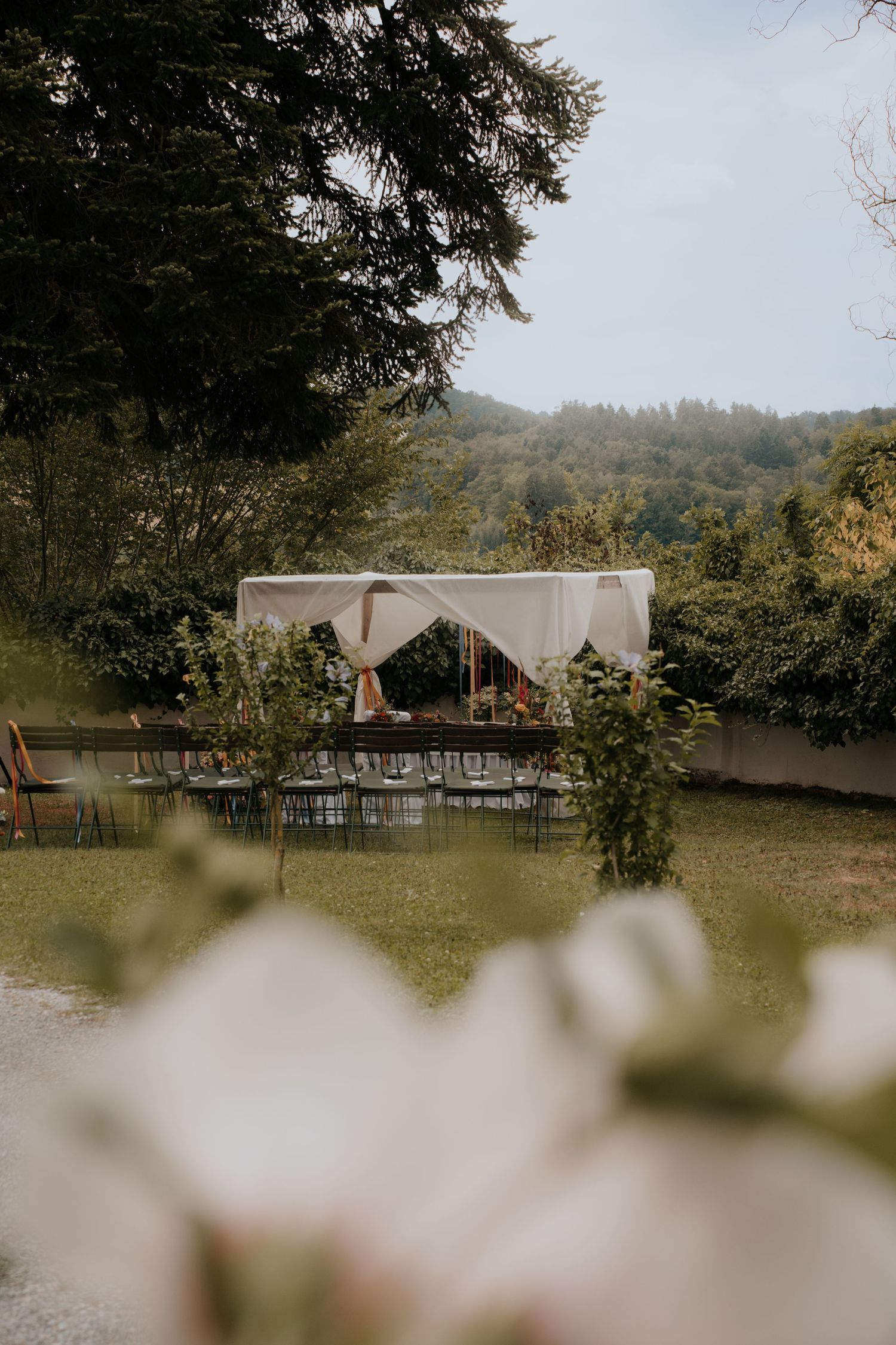 Elegant outdoor wedding ceremony setup with white canopy, rows of chairs, and lush green forest backdrop.