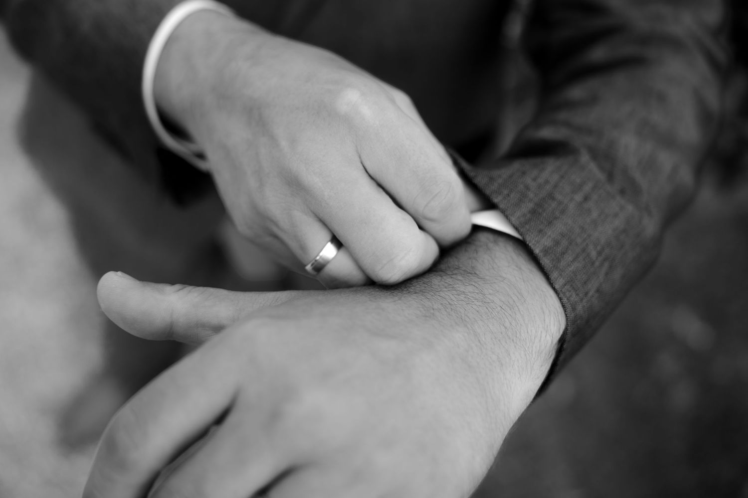 Black and white photo of a man adjusting another mans shirt cuff, wearing a wedding band.