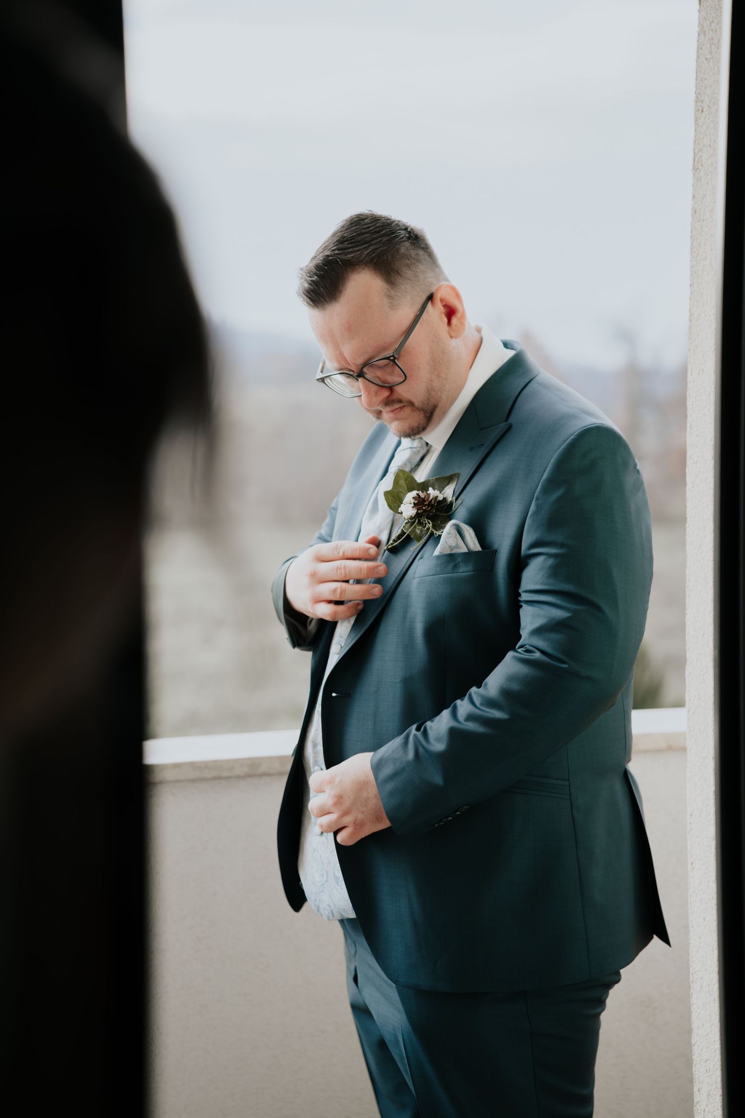 Groom in a navy suit adjusting his boutonniere before the wedding ceremony.