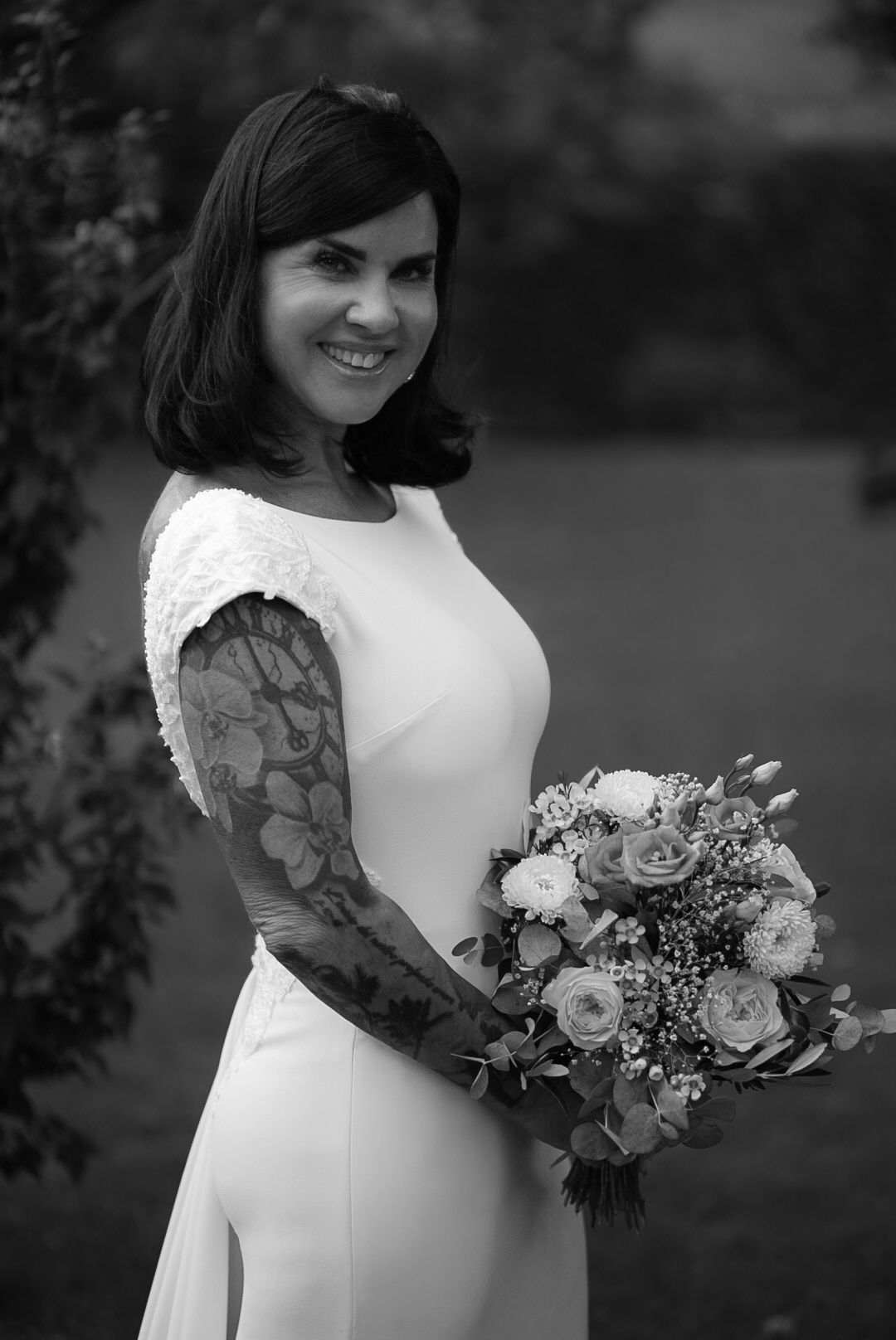 A bride in a white dress holds a bouquet featuring roses and greenery.