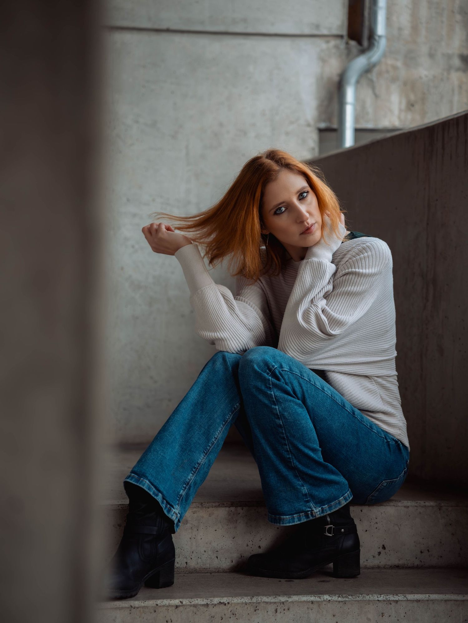 A portrait of someone sitting against a concrete wall in casual attire with natural lighting.
