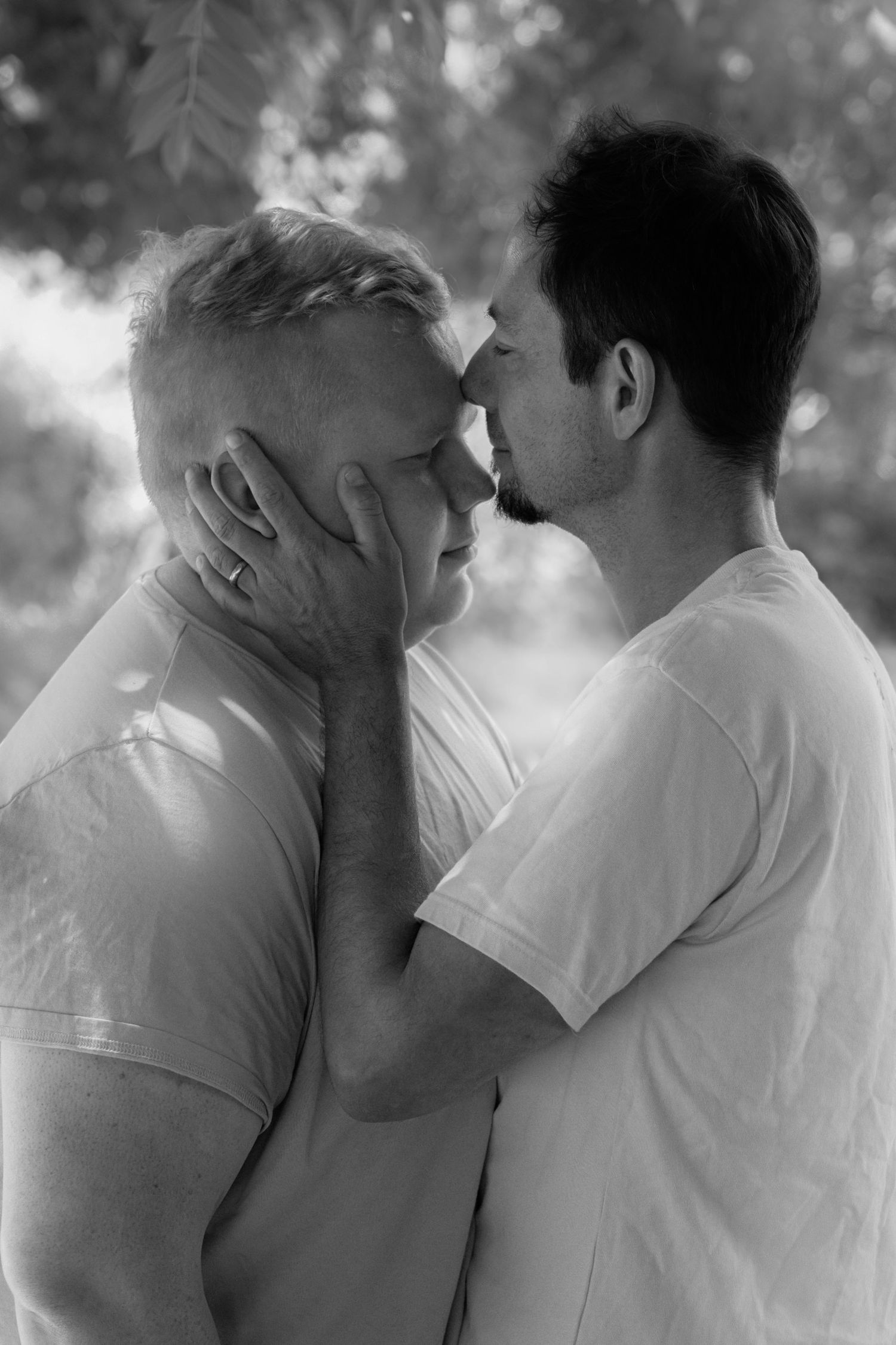 Black and white photo of two men sharing an intimate moment outdoors, one tenderly holding the others face.