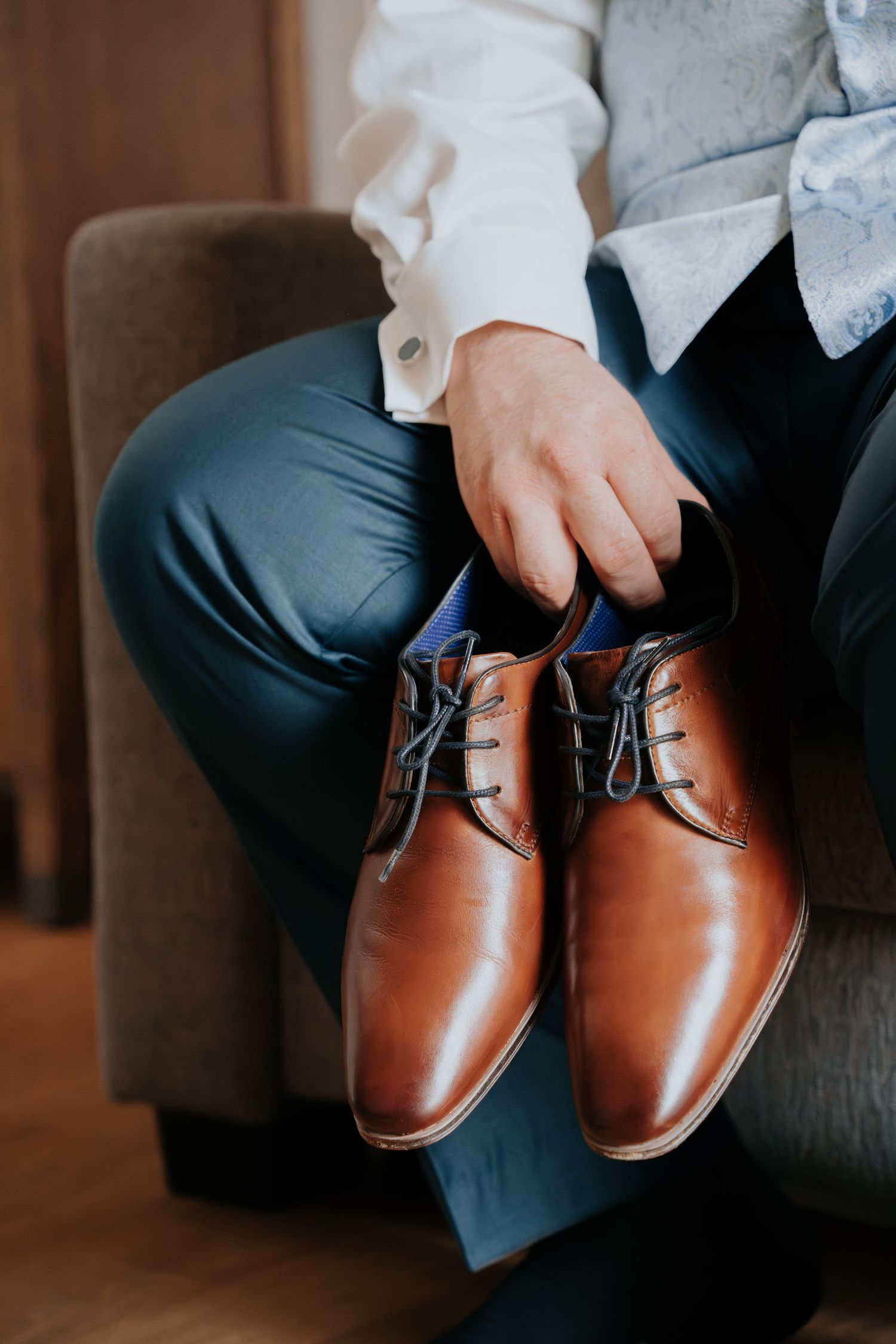 Brown leather dress shoes being held against dark formal pants.