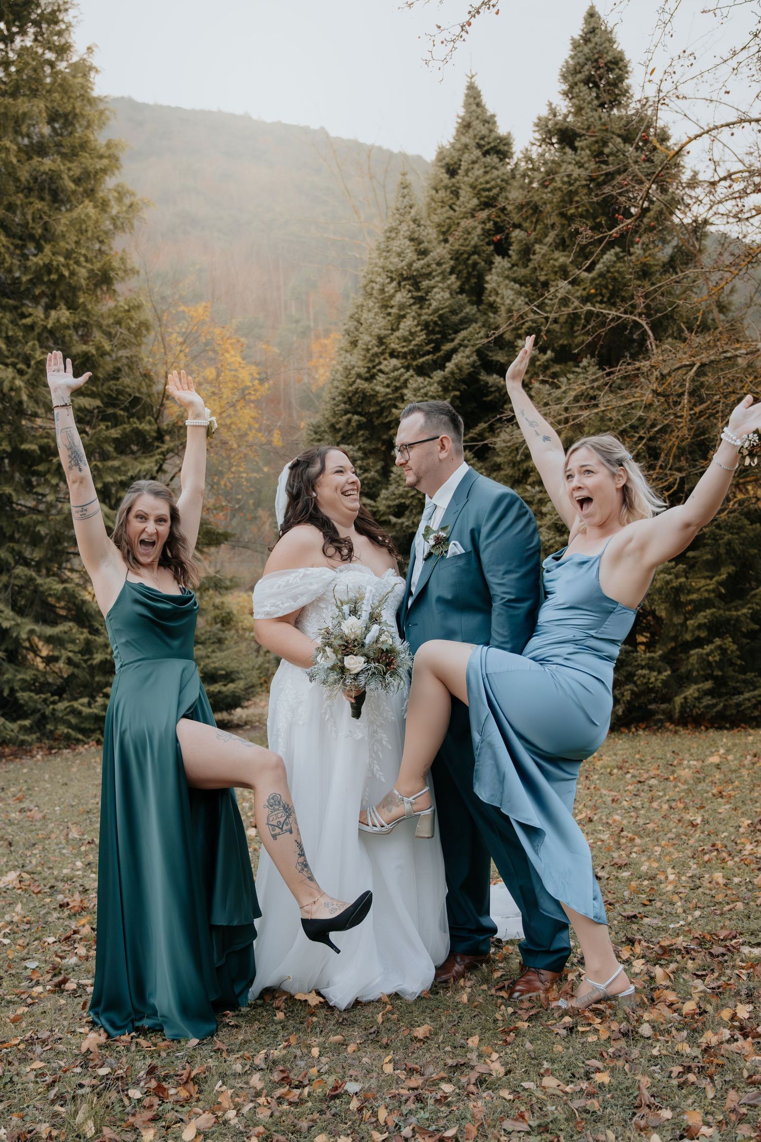 Wedding party in teal dresses and suits posing playfully in an autumn setting.