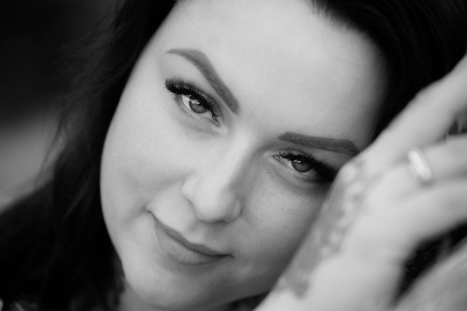 Black and white close-up portrait of a young woman smiling softly, with her hand raised near her face.