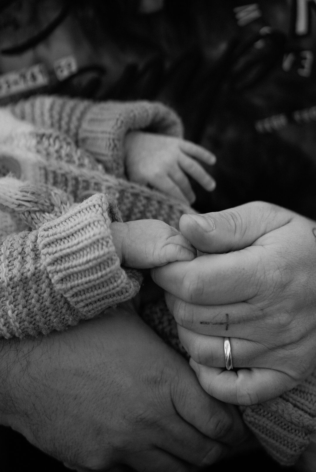Black and white photo of adult hands holding a newborn baby, with a wedding ring visible on one hand.