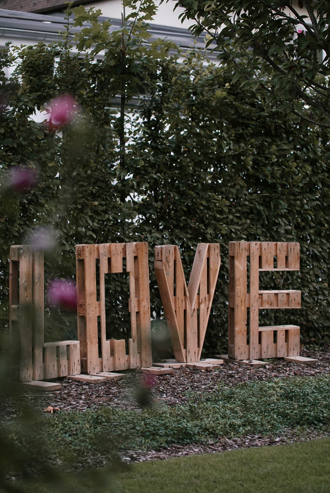 Large rustic wooden LOVE letters made from pallets displayed in a garden against green hedges.