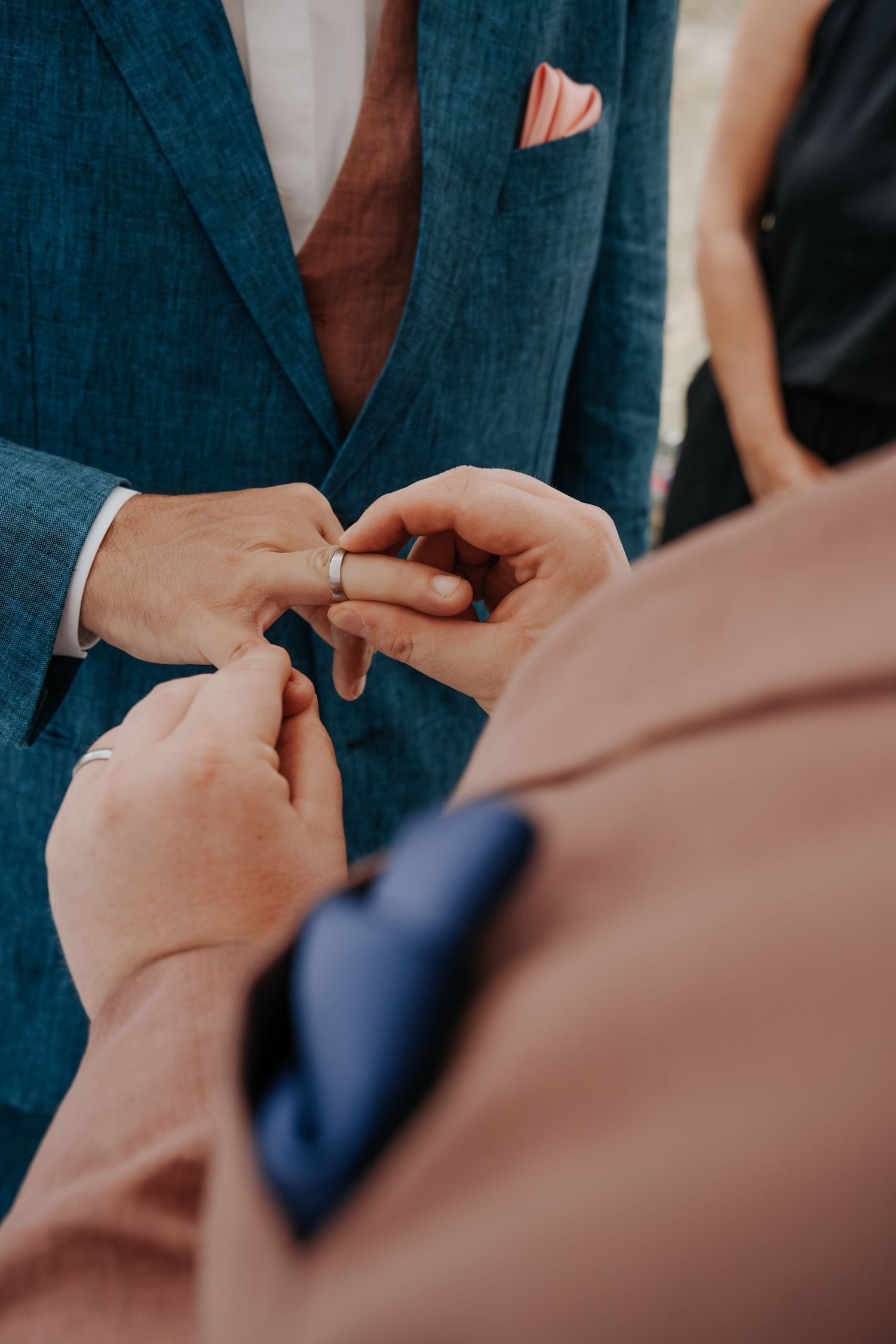 Close-up of groom placing wedding ring on partner's finger during ceremony, both wearing elegant suits.