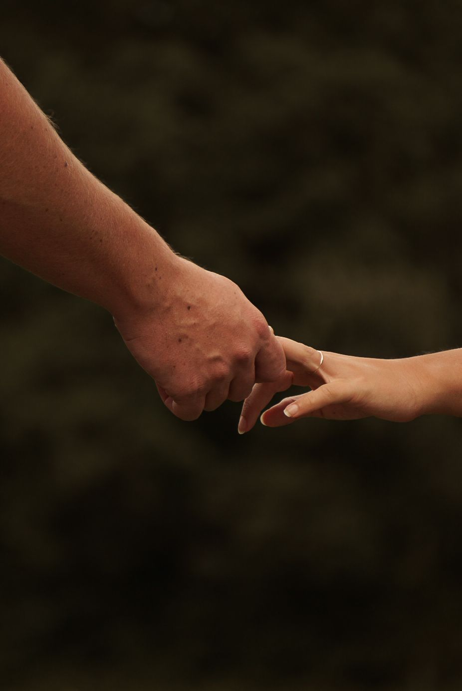 An elderly hand gently holding a younger person's hand against a dark background, symbolizing connection and care.