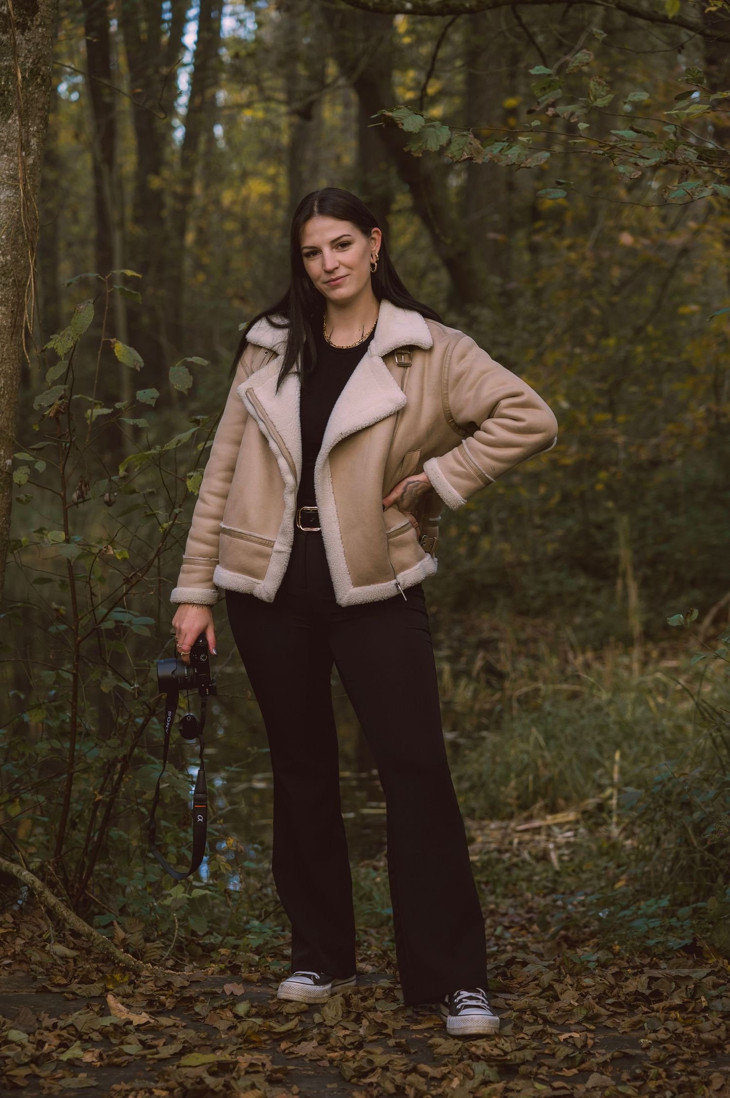 A casual autumn fashion photoshoot featuring a tan jacket and black pants in a forest setting.