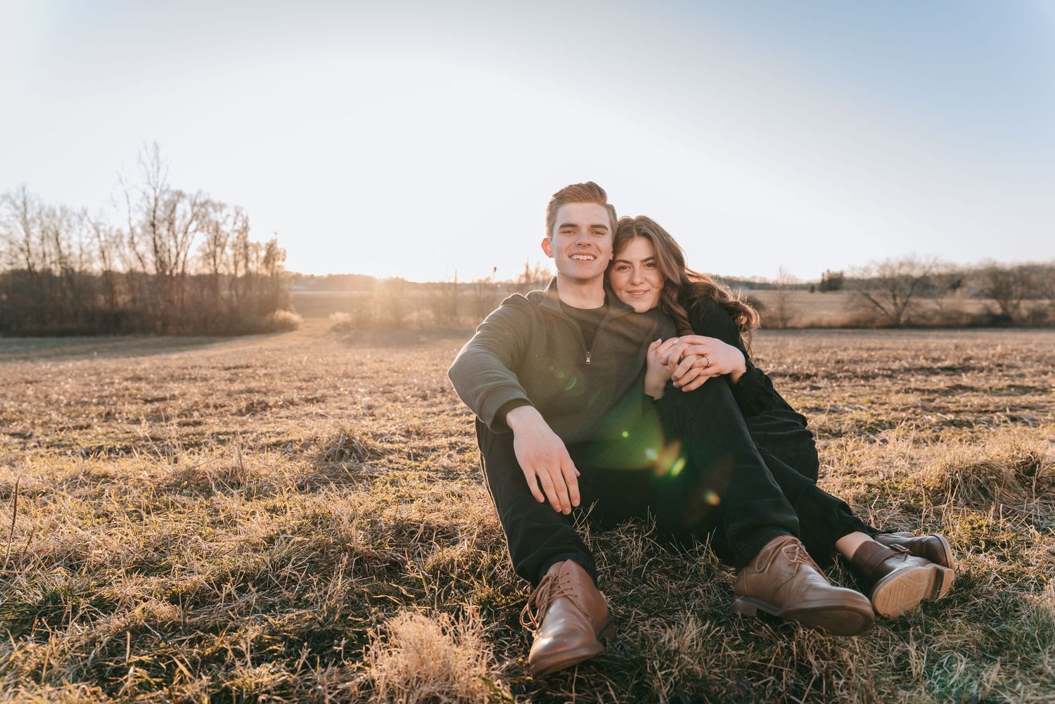 Engaged couple sitting together in a wide Finger Lakes landscape, soft sunset light and relaxed, joyful expressions