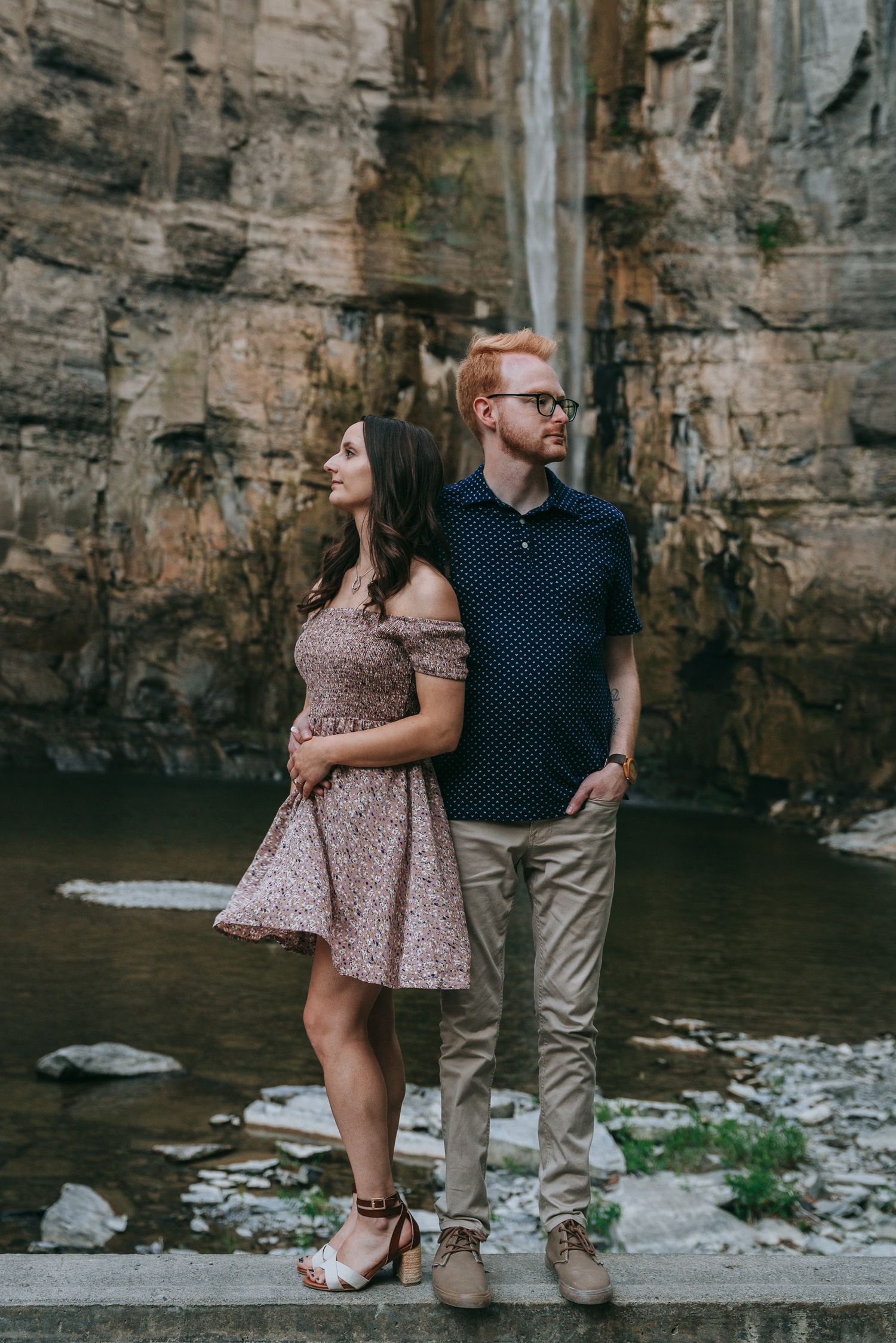 Engaged couple standing back to back in front of Taughannock Falls waterfall in the Finger Lakes region of New York
