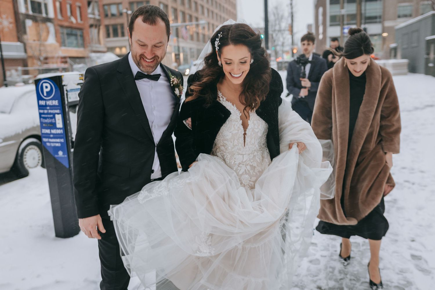 Bride and groom walking through snowy city street in Rochester NY, joyful winter wedding moment captured with documentary style photography