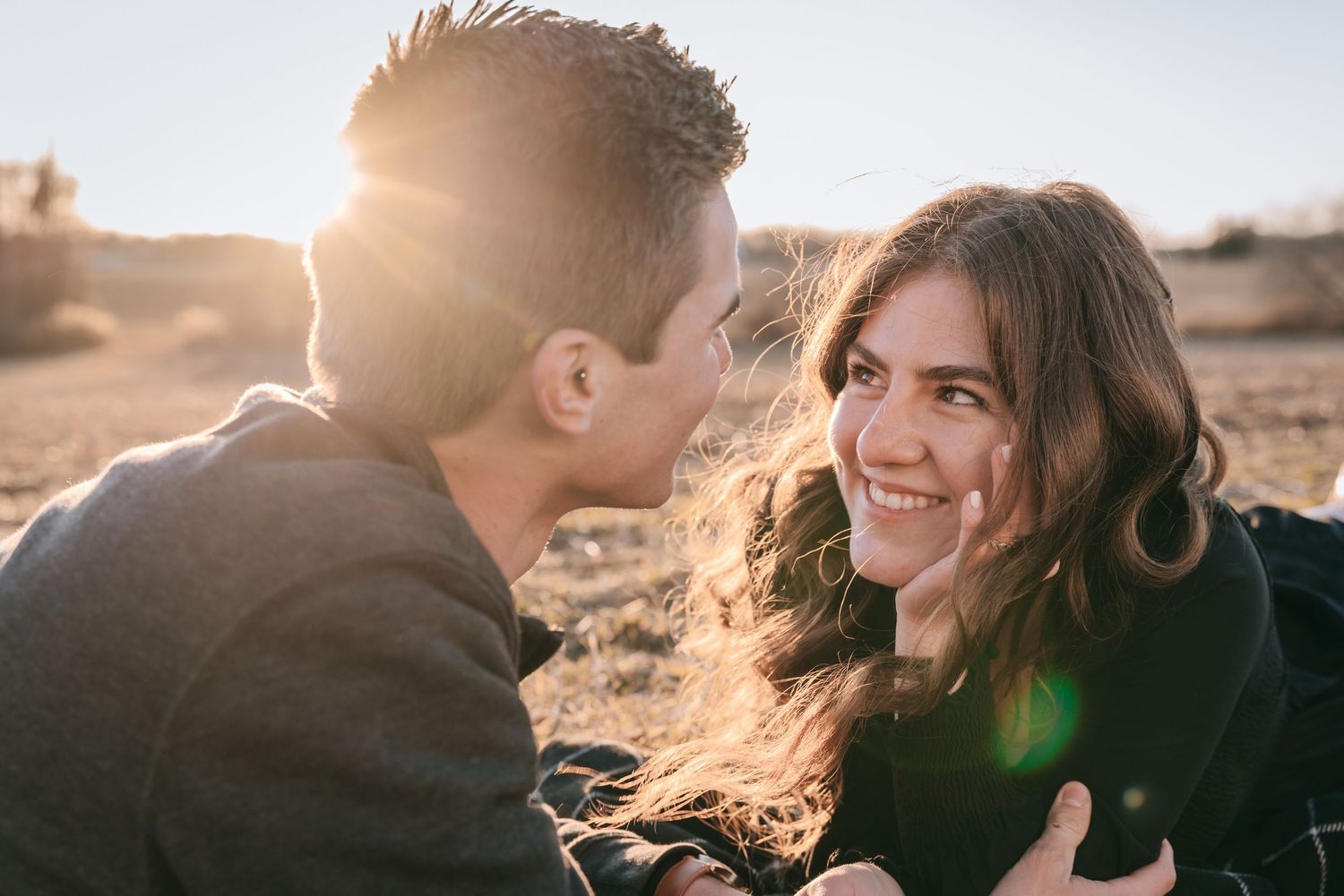 Romantic engagement portrait of a couple lying in a Finger Lakes field at sunset, sharing a quiet, intimate moment