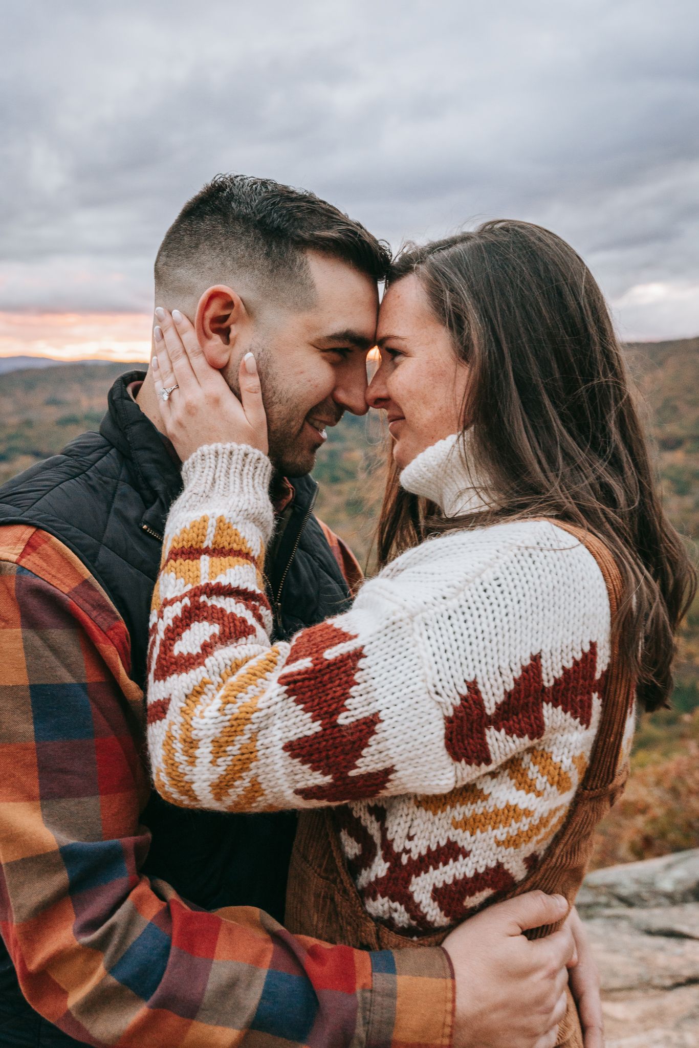 Intimate engagement photo of a couple touching foreheads on a mountain overlook in New Hampshire, with sweeping fall foliage behind them